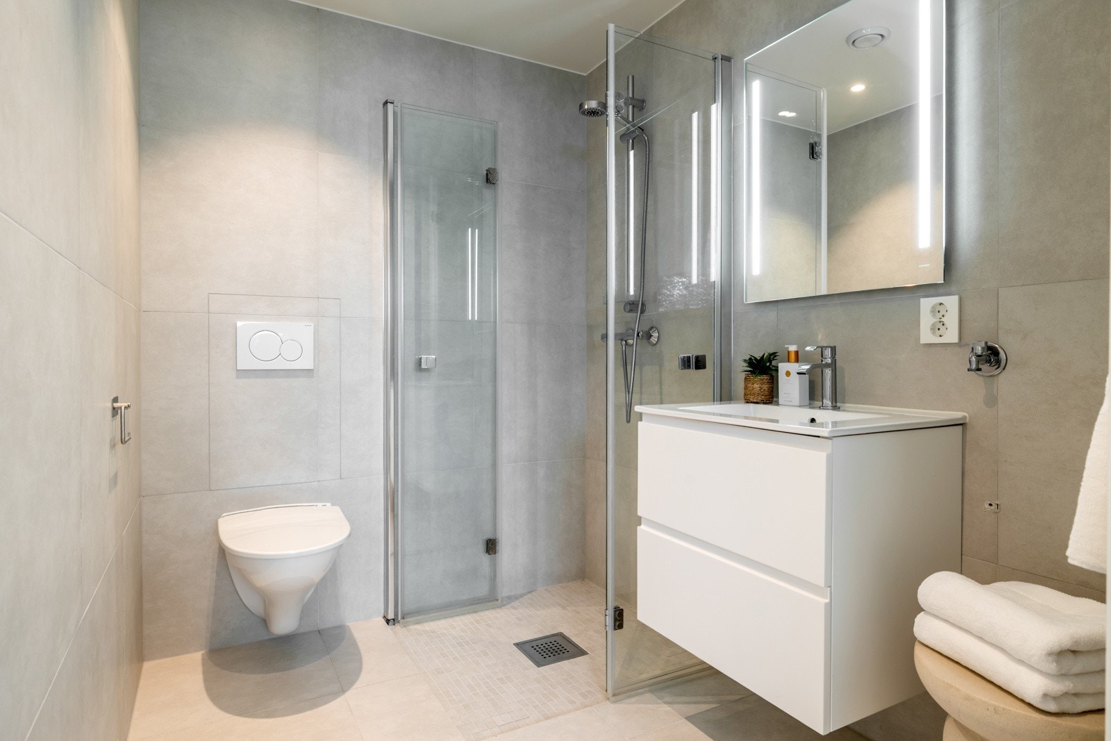 Badet i underetasjen er moderne og helfliset, med lyse fliser på både gulv og vegger som gir et rent og tidløst uttrykk. På dette badet er det lagt opp til ekstra vaskemaskin, noe som gir mulighet for å kunne etablere hybel. Galleribilde