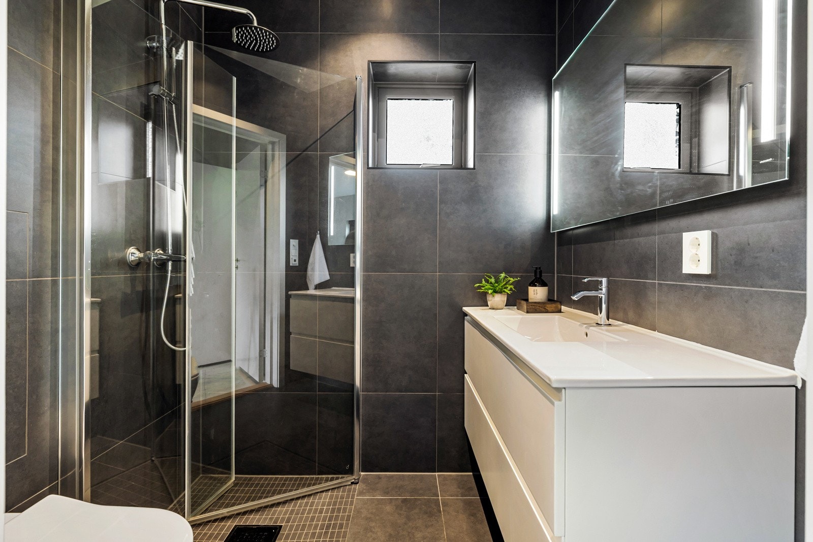 Rommet er utstyrt med vegghengt toalett, dusjhjørne med innfellbare glassdører, servantinnredning med skuffer og speil med integrert belysning. Det er elektriske varmekabler i gulvet som gir en behagelig temperatur. Galleribilde