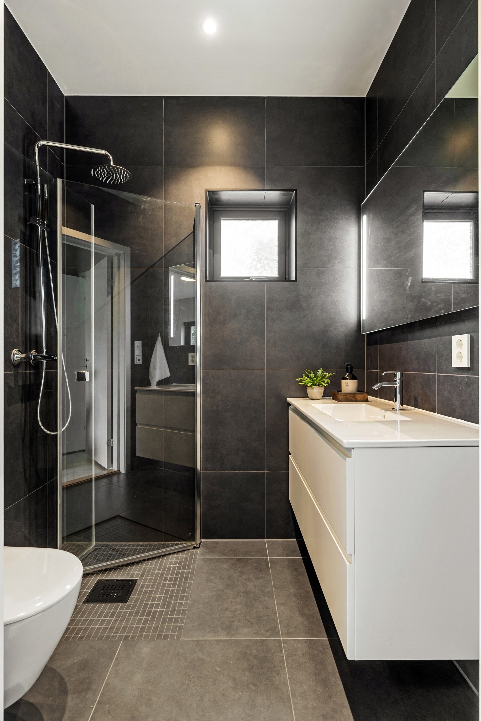 Badet tilknyttet hovedsoverommet i 2. etasje er moderne og helfliset med mørke fliser på gulv og vegger som gir et eksklusivt uttrykk. Galleribilde