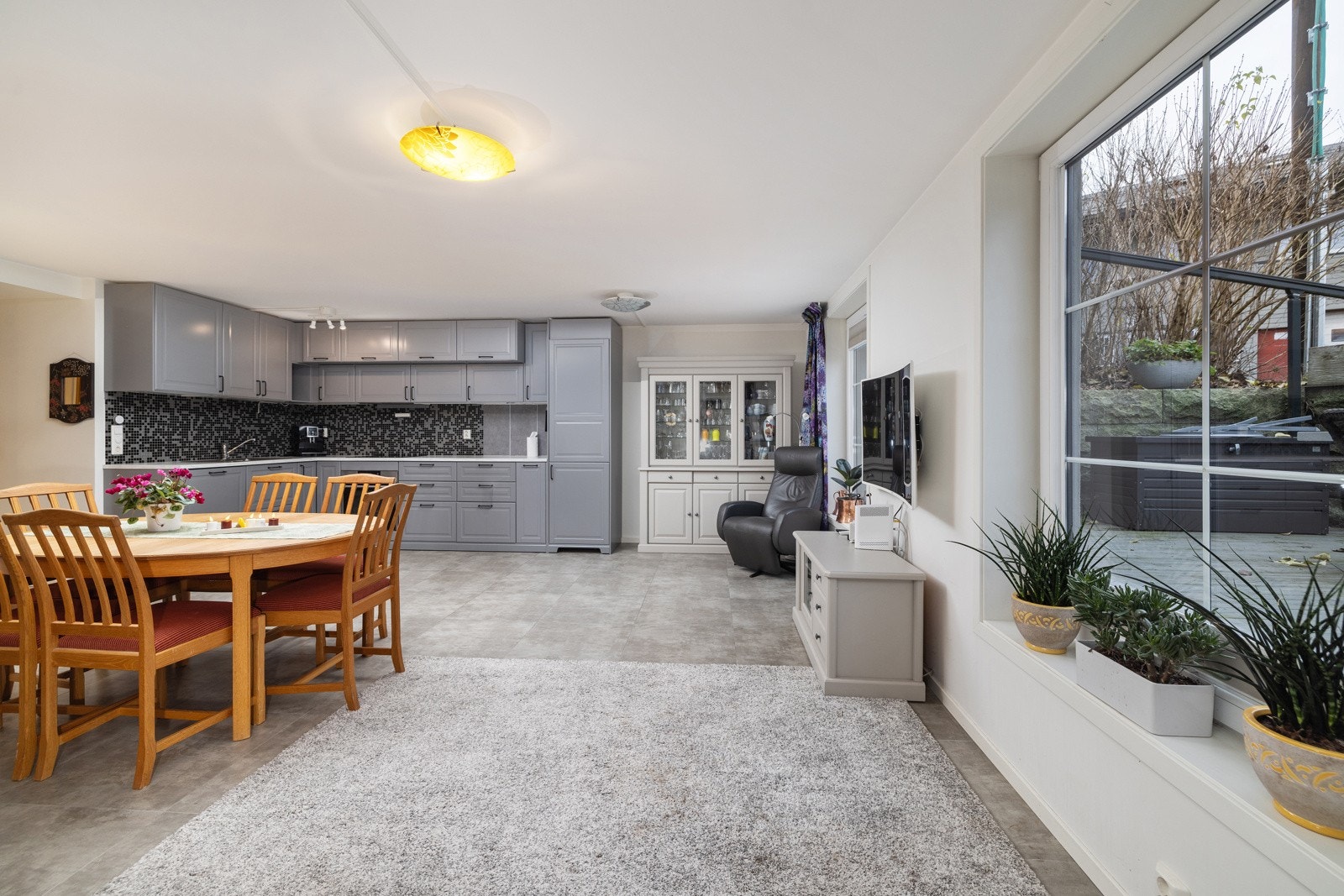 Det er kjøkkeninnredning med grå profilerte fronter, laminat benkeplate med kum og mosaikkfliser over benken. Galleribilde