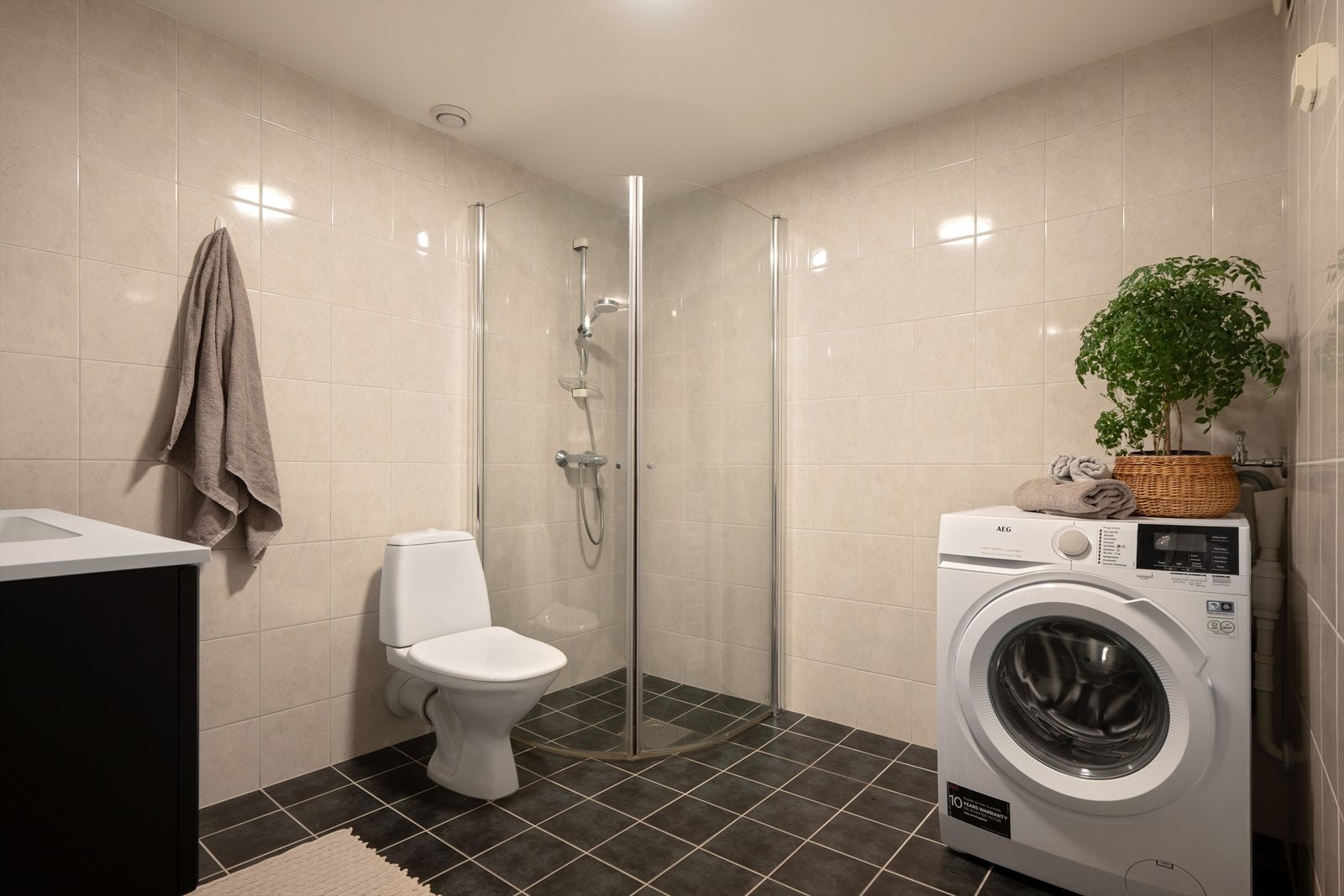 Bad fra 2009 med servantskap, speil og taklampe fra 2025: Flislagte vegger og gulv med varmekabler, samt et godt areal. Galleribilde