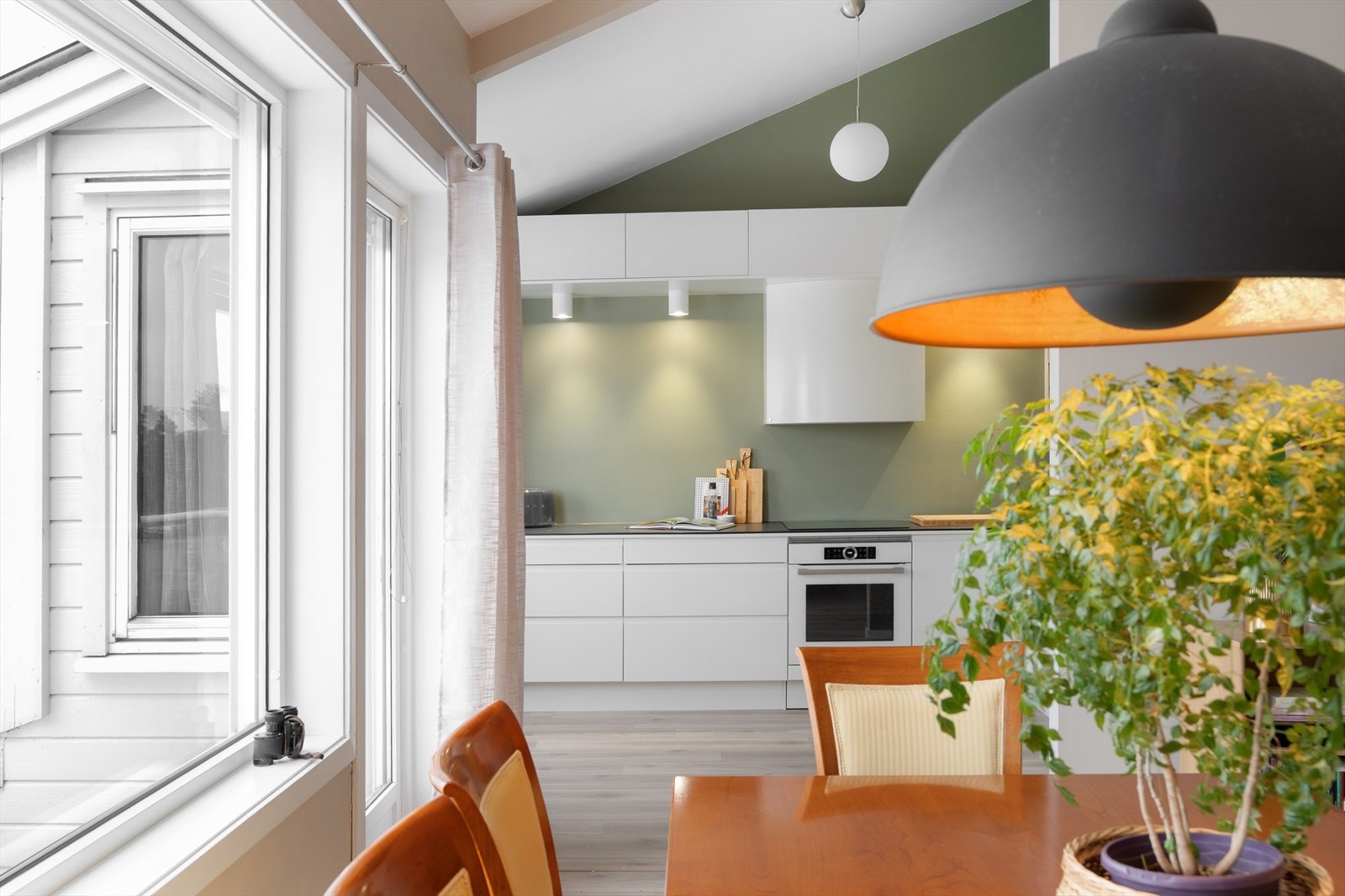 Kjøkkenet har hvite, slette fronter og laminat benkeplate fra 2020, med integrerte hvitevarer som kjøl/frys og ovn. Galleribilde