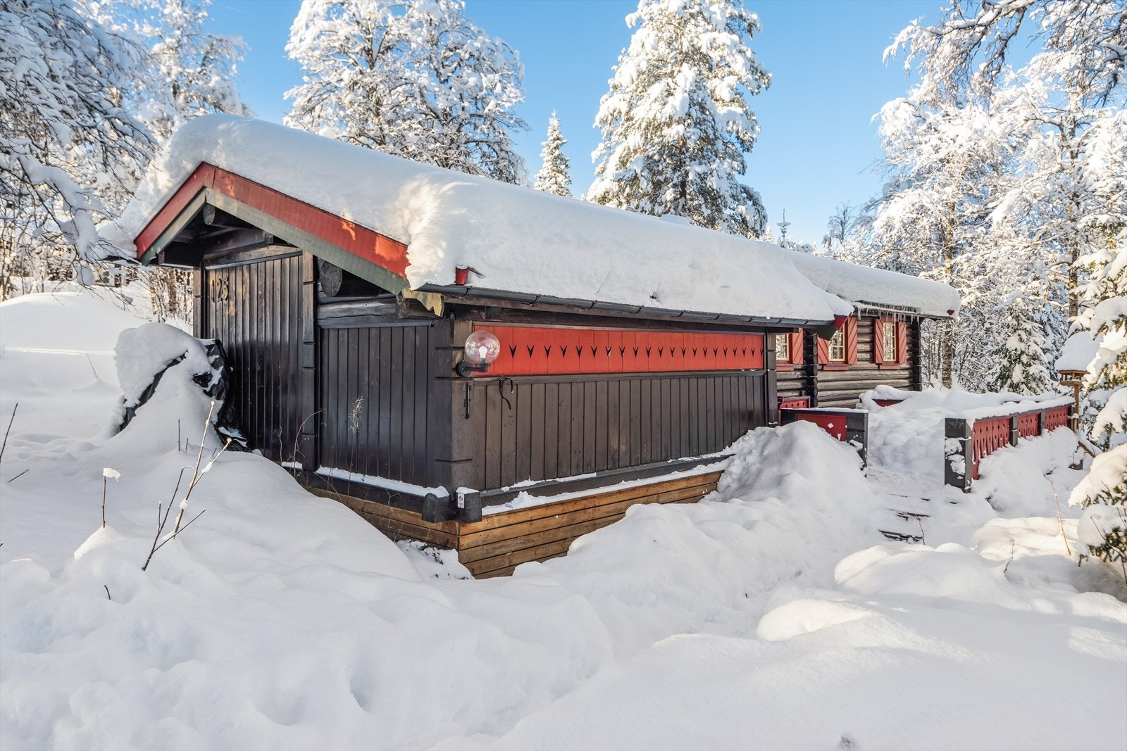 Hytta ligger usjenert til, omgitt av snøtunge trær. Galleribilde