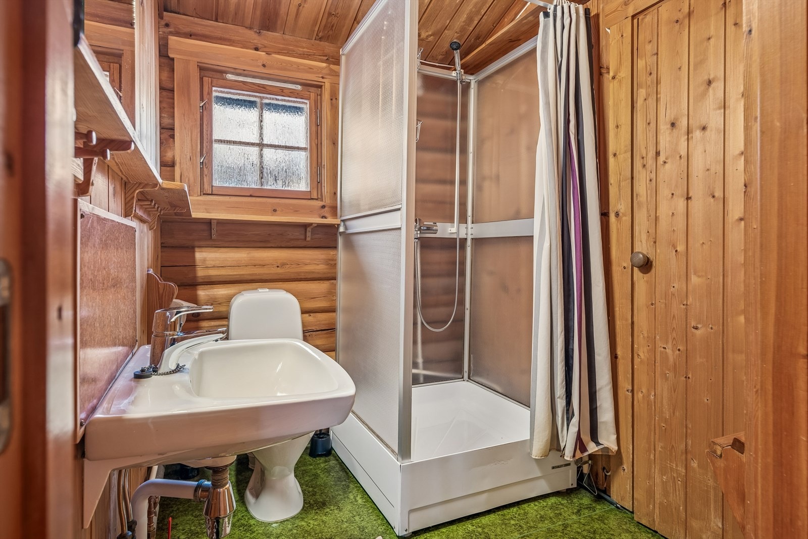 Bad fra byggeår med behov for oppgradering. Enkelt utstyrt med toalett, servant og dusjkabinett. Dør inn til badstua. Galleribilde