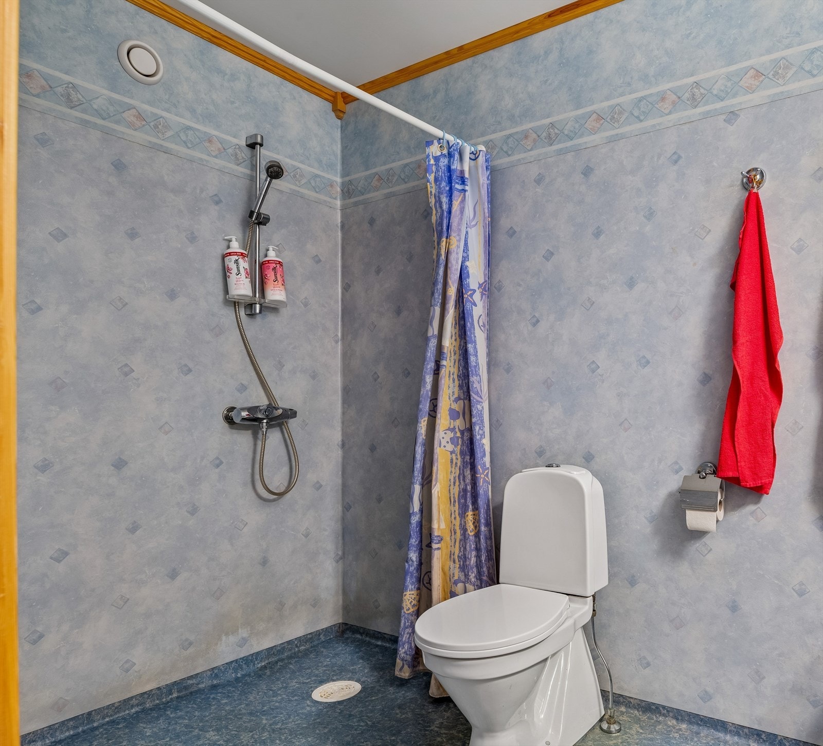 Badet er utstyrt med gulvmontert toalett og dusj. Overflatene har våtromsbelegg på vegger og gulv. Galleribilde