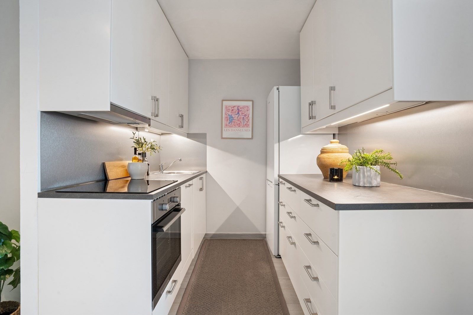 Kjøkkenet har en moderne innredning med glatte, hvite fronter og en laminatbenkeplate med nedfelt stålkum. Galleribilde