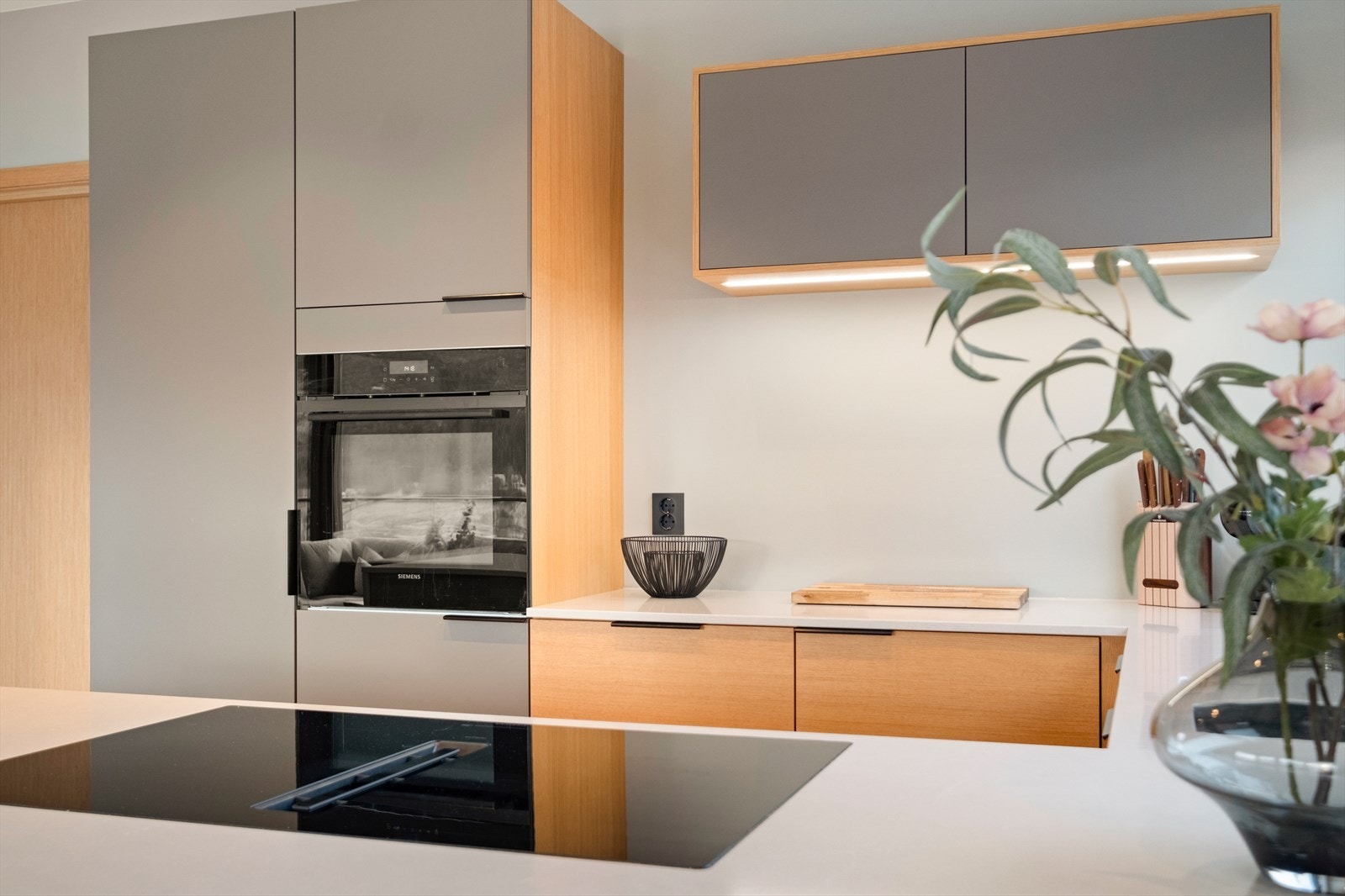 Grå fronter og treverk kombineres for en moderne kjøkkeninnredning. Galleribilde