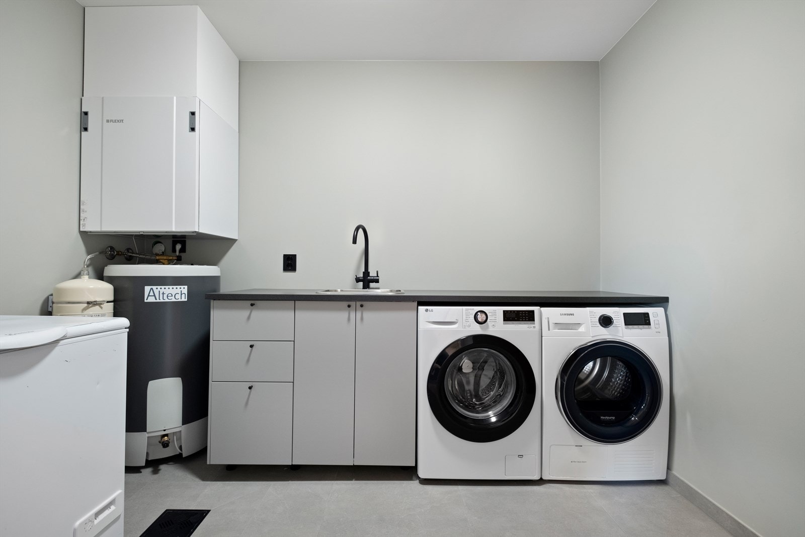 Praktisk vaskerom med flislagt gulv og plass til både vaskemaskin og tørketrommel. Galleribilde