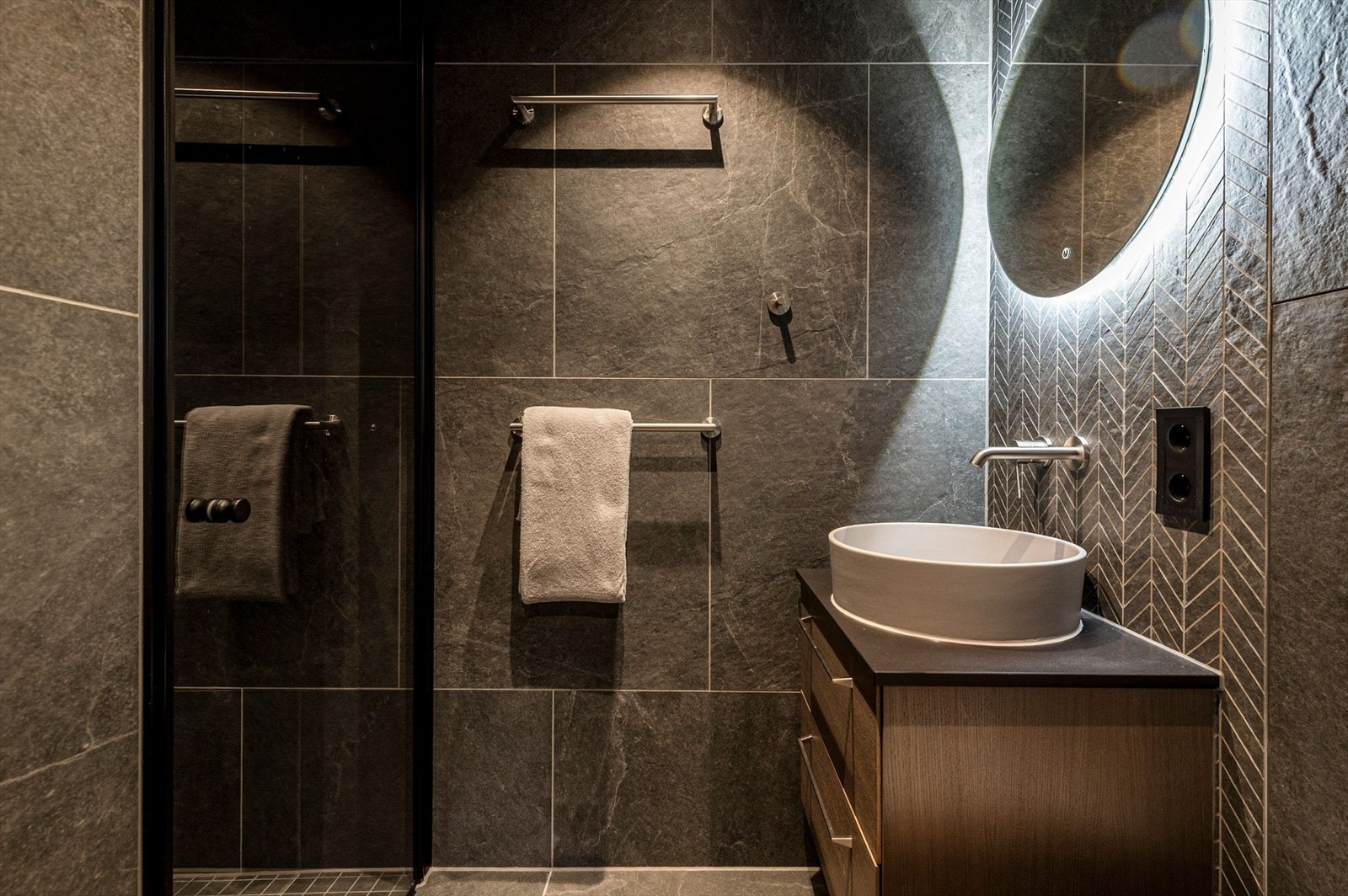 Bad i tilknytning til hovedsoverom med dusjhjørne med glassdører, servant med underskap, speil og belysning. Veggmontert toalett. Galleribilde