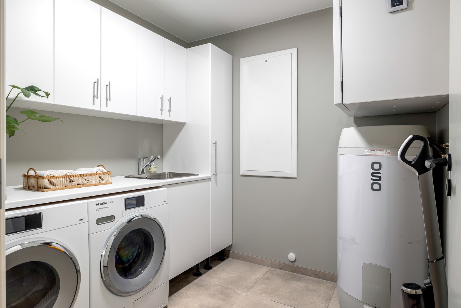 I underetasjen ligger et funksjonelt vaskerom med flislagt gulv med varmekabler og malte veggflater. Rommet er utstyrt med vaskeromsinnredning, nedfelt vaskekum og en nisje med plass til både vaskemaskin og tørketrommel. Galleribilde