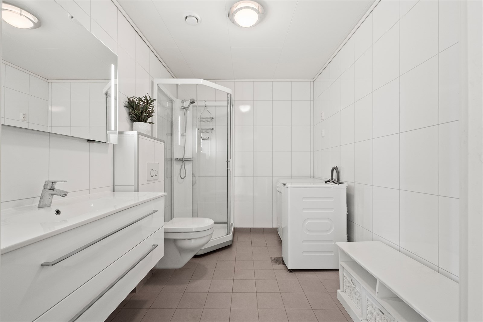 Lyst og romslig bad utstyrt med vegghengt wc, dusjkabinett, opplegg til vaskemaskin, heldekkende servant med underskap og speil med integrert lys og strømuttak. Galleribilde