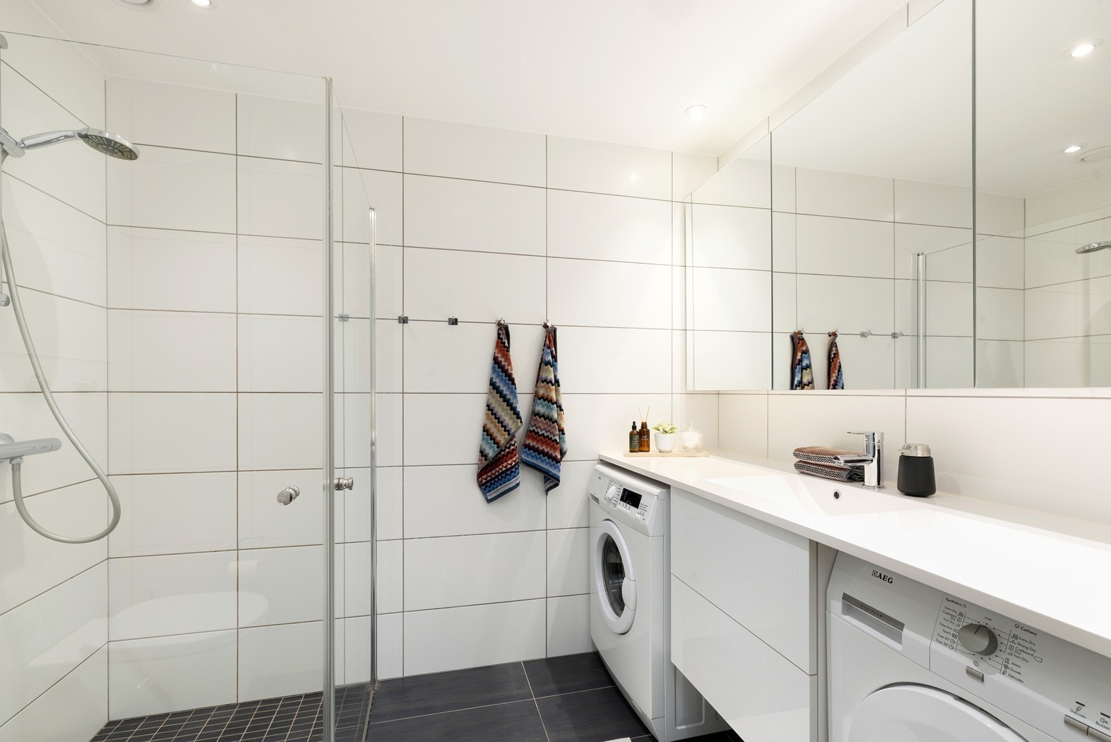 Flott fliselagt bad med dusjvegger, HTH innredning, vegghengt toalett samt opplegg til vaskemaskin og tørketrommel. Galleribilde