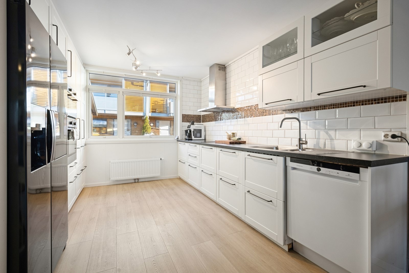 Innredningen har folierte skrog med profilerte fronter i lys utførelse og benkeplate i laminat og fliser på vegg over benkeplate Galleribilde