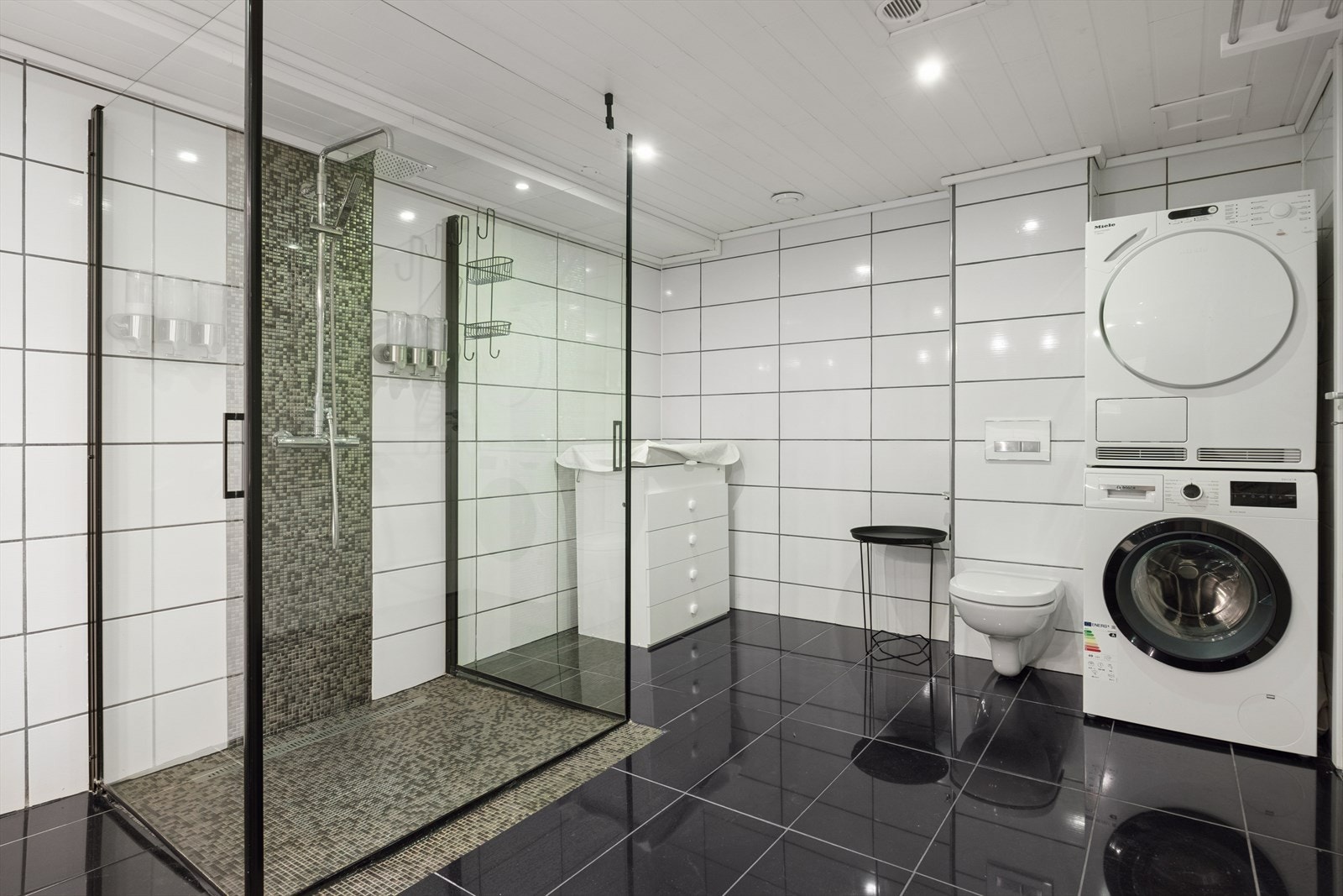 Delikat flislagt baderom fra 2013 på 12,1 m² med innfellbar dusj av god størrelse, utstyrt med blant annet vegghengt toalett og opplegg til vaskemaskin og tørketrommel. Himlingen er malt. Galleribilde