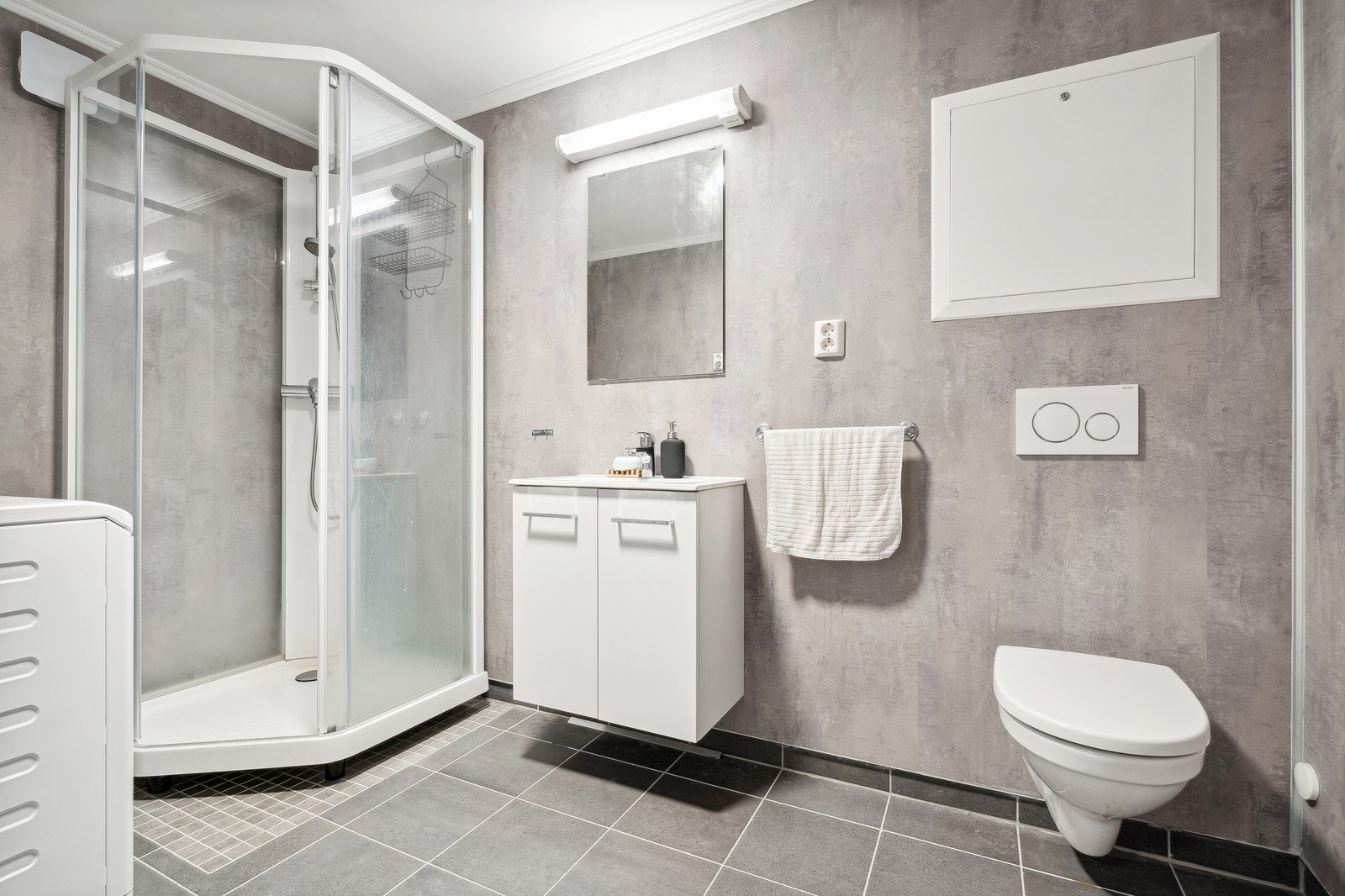 Pent bad med dusjkabinett, vegghengt toalett, servant og innstallert vaskemaskin. Galleribilde