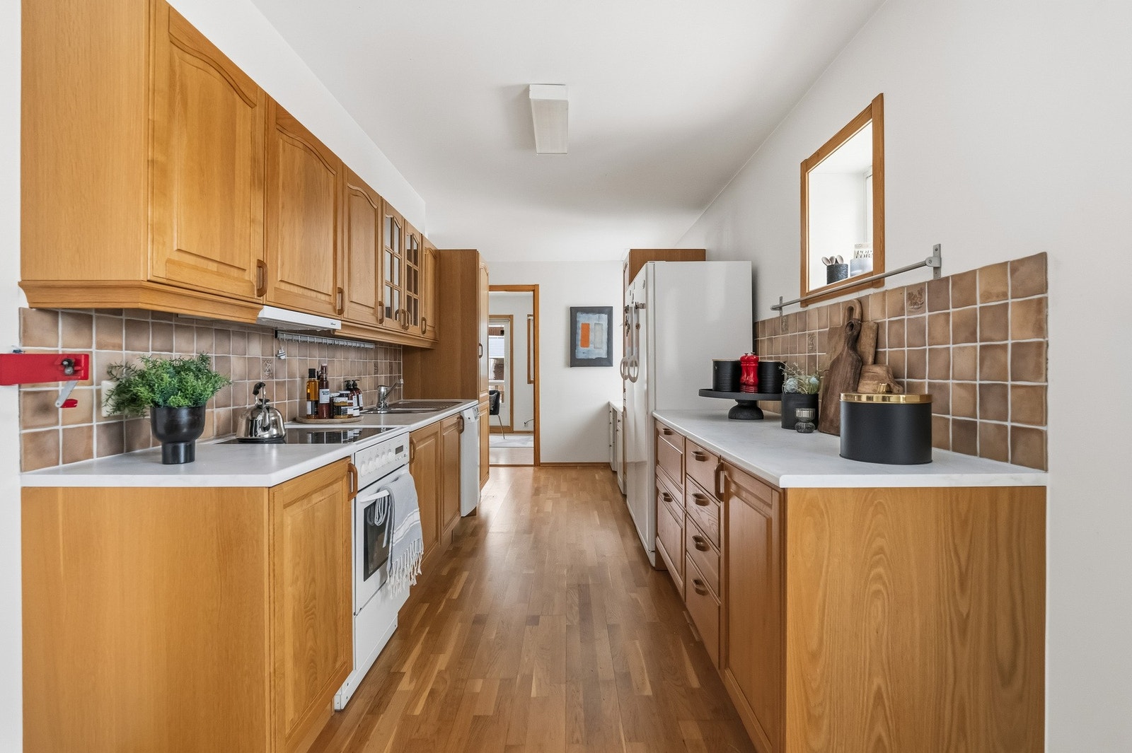 Kjøkkeninnredning med profilerte fronter og enkelte overskap med glassfronter. Fliser på vegg over benkeskap og laminat benkeplate med nedfelt kum i rustfritt stål. Det er opplegg for oppvaskmaskin. Galleribilde