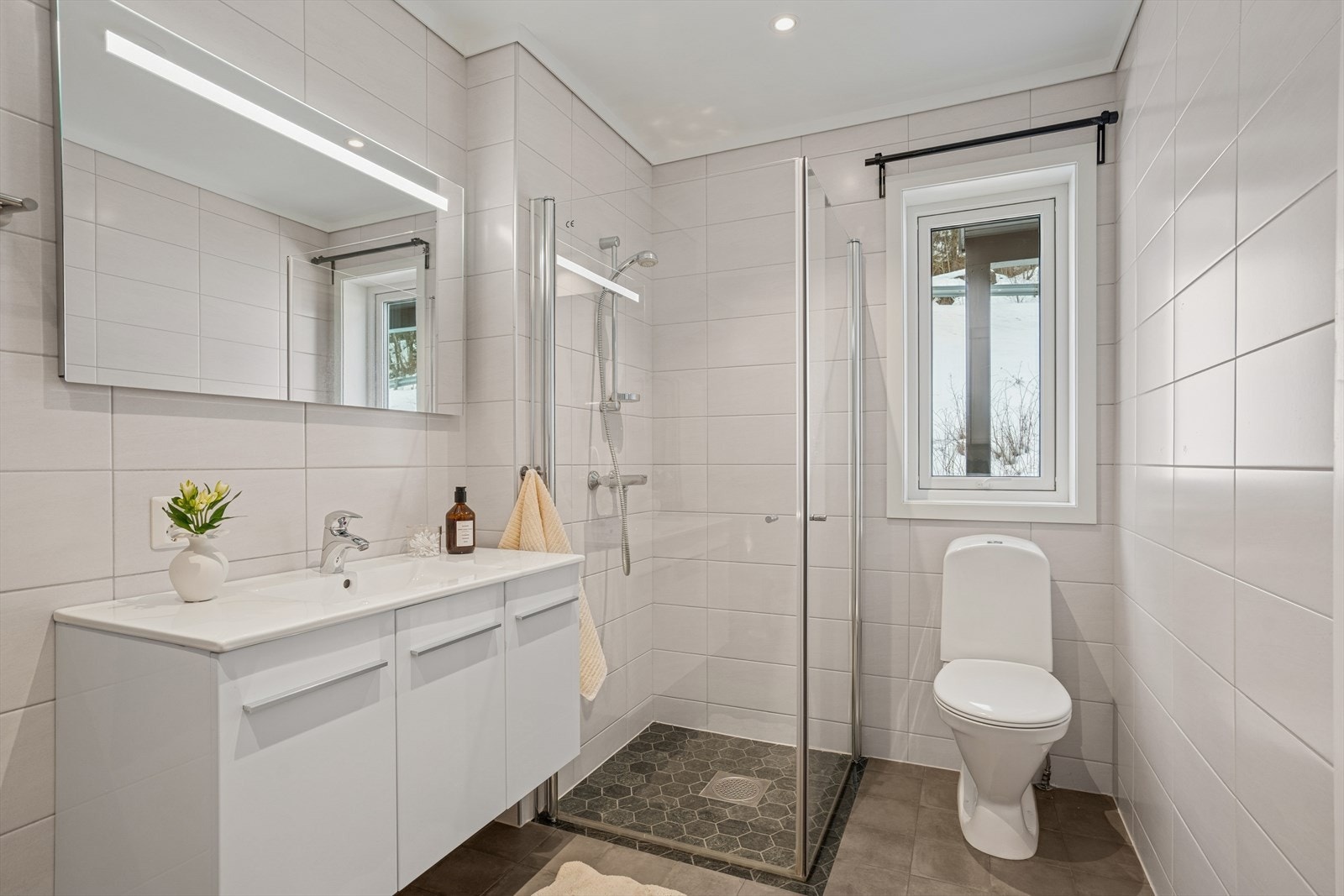 Tidløst og delikat bad fra 2020. Badet har god størrelse og fungerer som kombinert vaskerom. Gulvet er flislagt med varmekabler, og veggene har hvite, tidløse fliser. Galleribilde