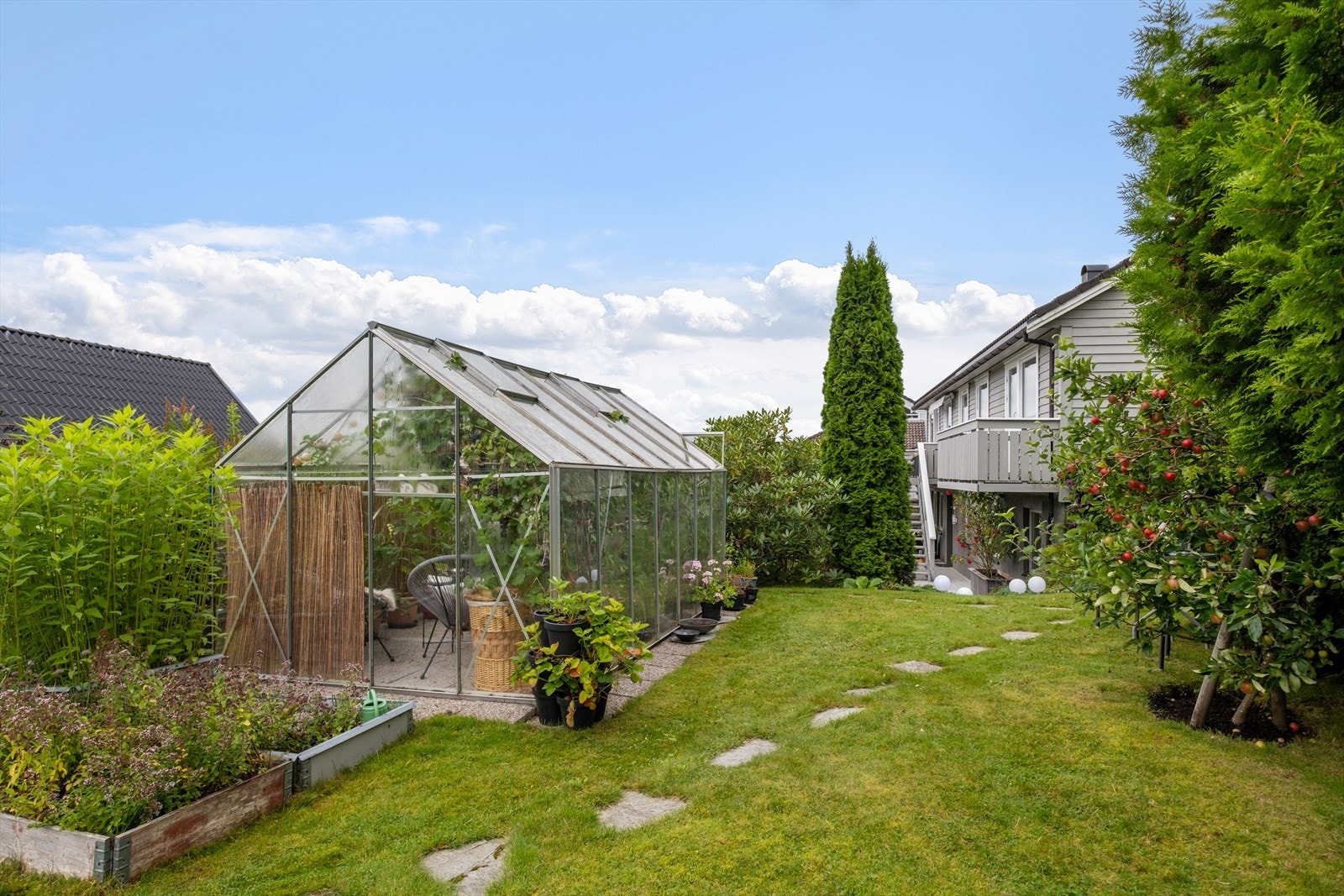 Drivhuset ligger i en velstelt hage med gangstier og beplantning. Galleribilde