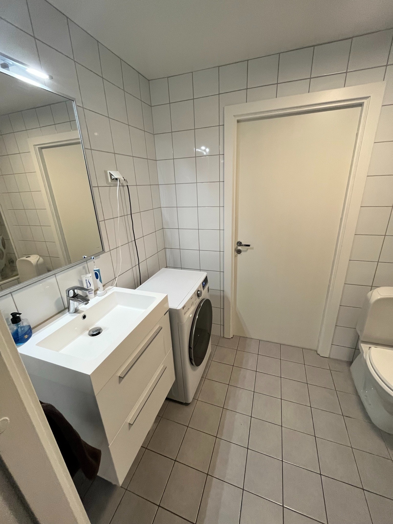 Pent flislagt baderom med moderne servantmøbel og praktisk vaskemaskin. Galleribilde