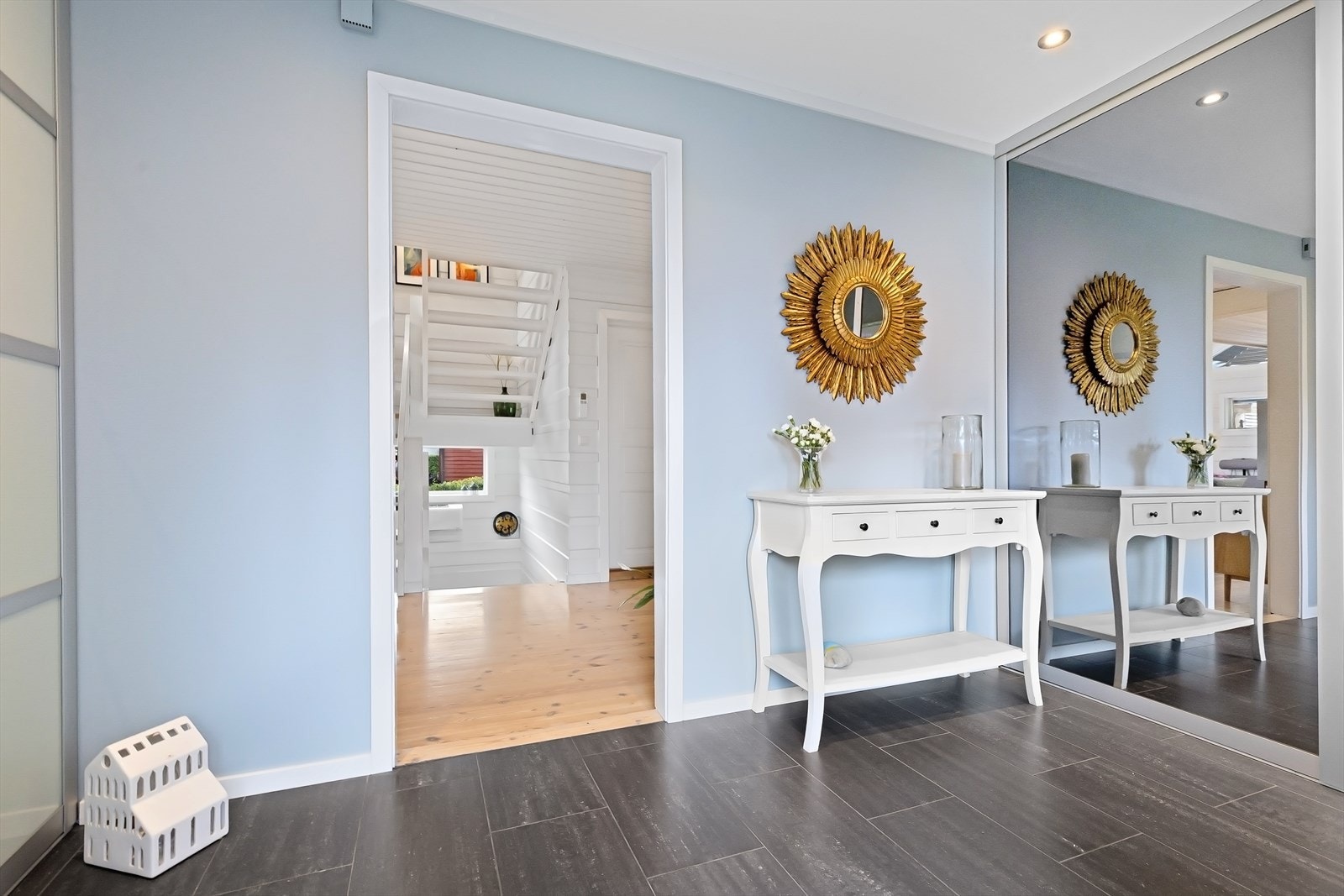 Boligen har en stor og innbydende gang, malt i lyse farger og med fliser på gulv Galleribilde