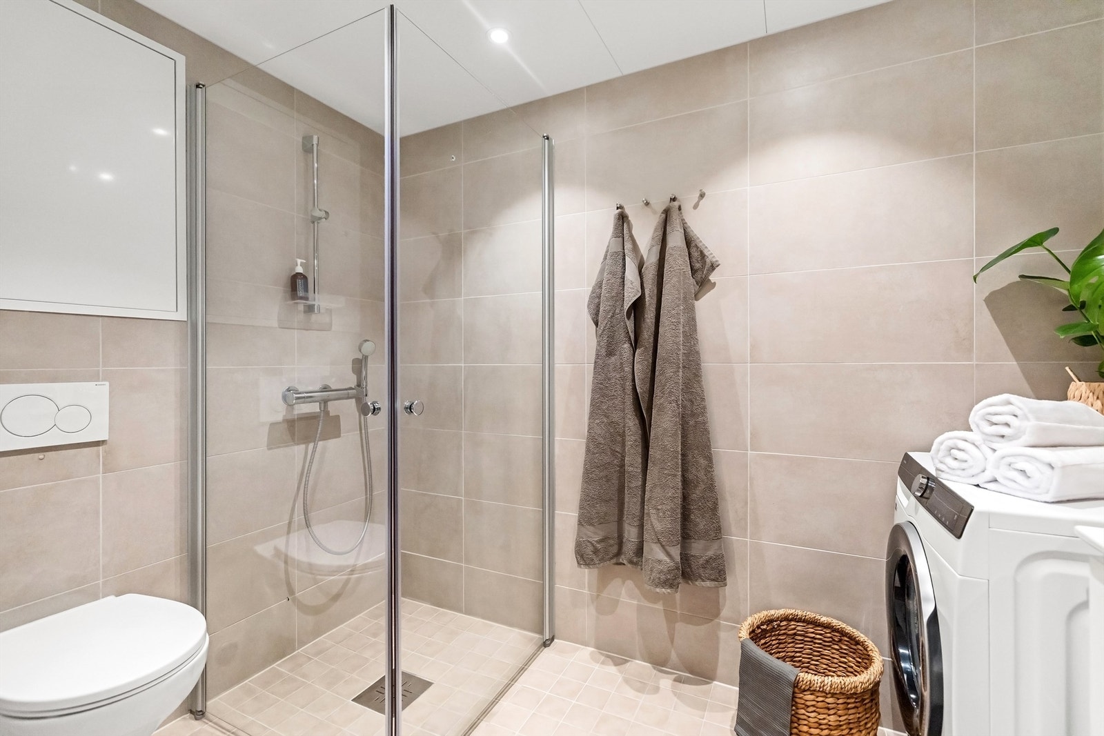 Badet inneholder vegghengt innredning med ovenpåliggende servant, speil med overlys, dusjsone med innfellbare glassdører samt vegghengt toalett. Galleribilde