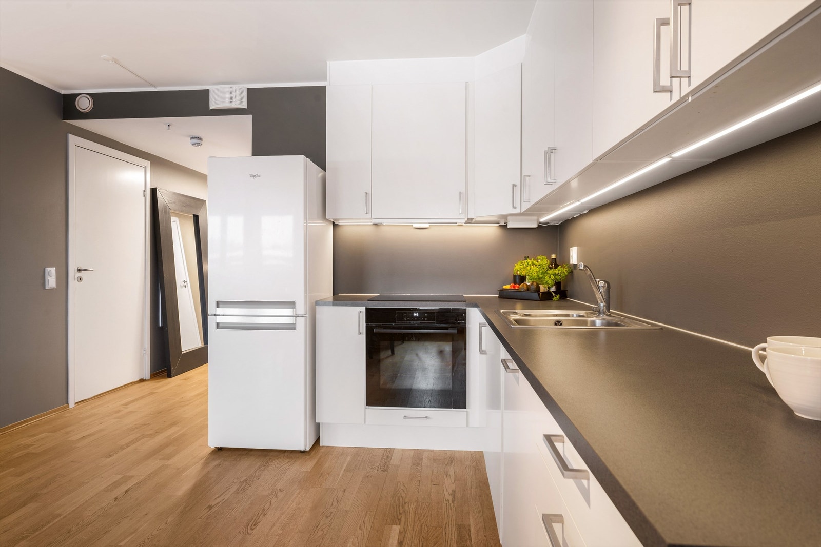 Kjøkkeninnredning med hvite, slette fronter og benkeplater av laminat med nedfelt oppvaskkum og ettgreps armatur Galleribilde