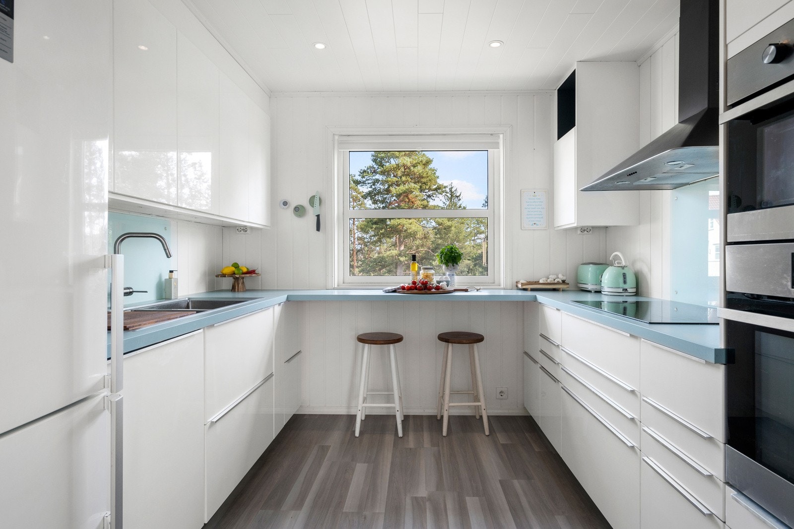 Et praktisk utformet kjøkken med innredning langs tre vegger og plass til stoler ved vinduet. Varmefolie i gulvet. Galleribilde