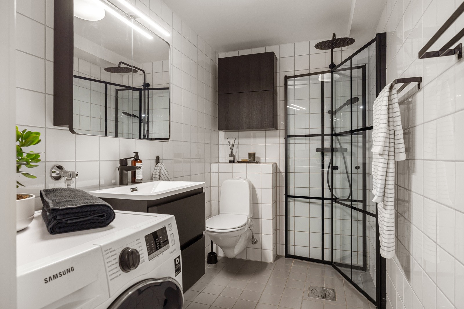 Moderne baderomsinnredning fra 2025 med skuffer og heldekkende servant, speilskap med belysning over. I hjørnet er det plass og opplegg for vaskemaskin, samt tørketrommel over om ønskelig. Galleribilde