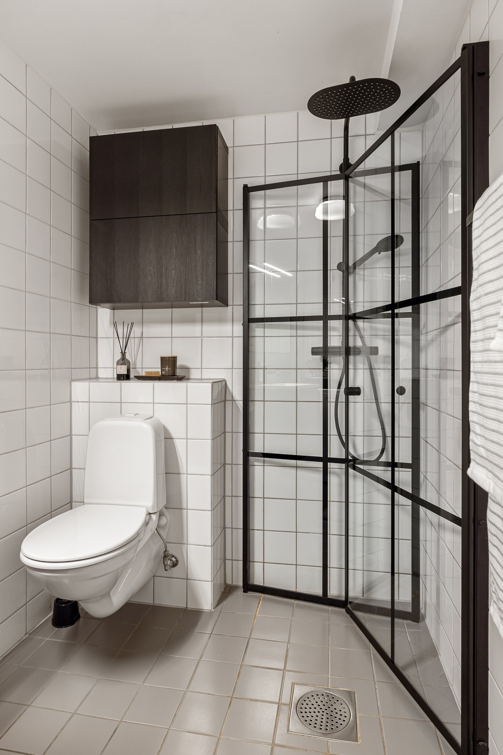 Dusjhjørne med stilige innfellbare glassdører og sort armatur med både hånd- og regnfallsdusj. Baderommet er også utstyrt med veggmontert toalett. Galleribilde