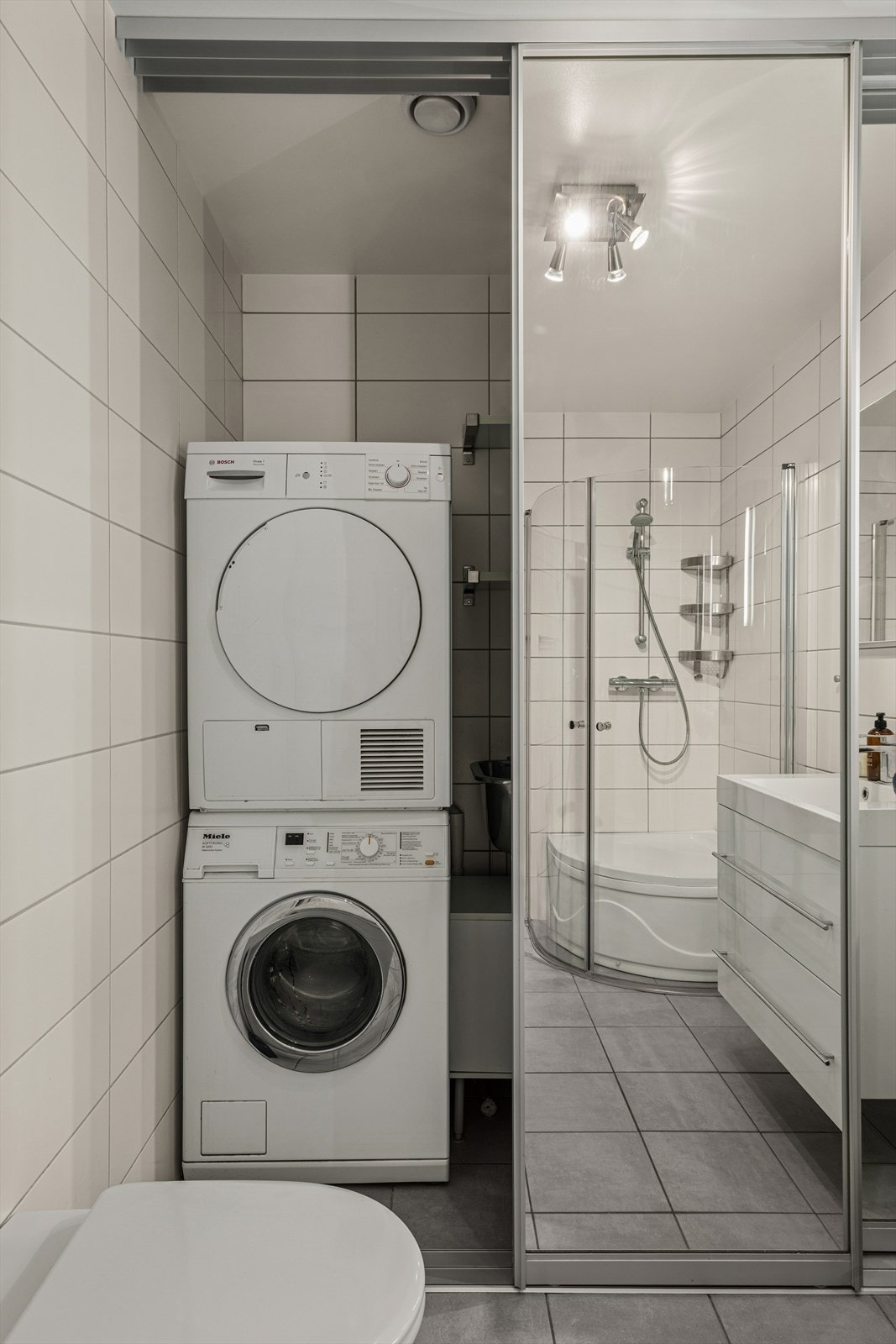 Dusjsonen har dusj montert på vegg med glassdører, og et løst badekar som enkelt kan tas ut ved behov. Rommet har opplegg for vaskemaskin, og speilskyvedører som praktisk skjerm mellom baderomsdelen og vaskesonen. Ventilasjonen skjer via avtrekksventil. Galleribilde