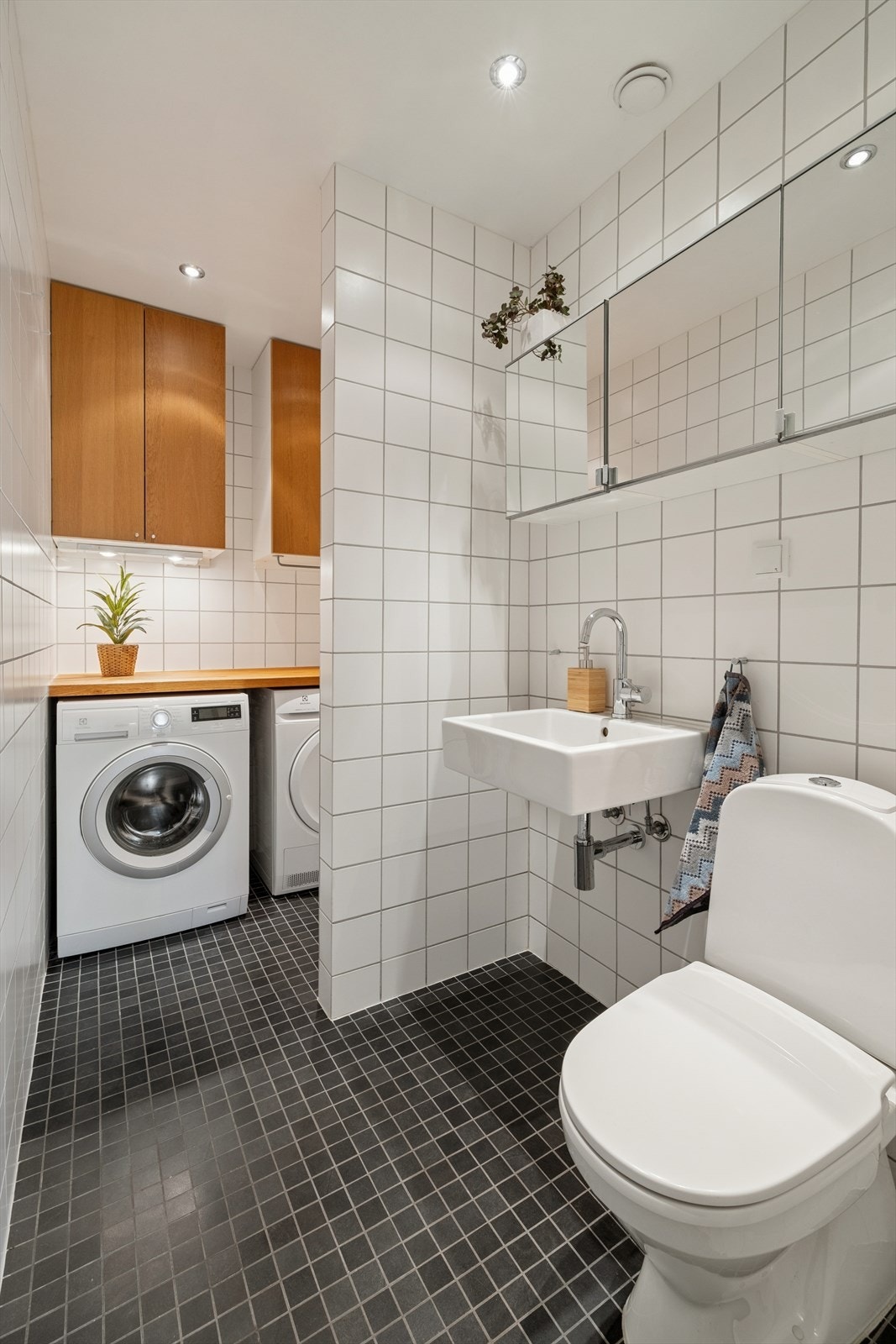 Vaskerommet har flislagte gulv og vegger samt elektriske varmekabler for god komfort. Malt himling med downlights gir et moderne uttrykk. Rommet er praktisk innredet med servant, toalett, opplegg for vaskemaskin og benkeplate for effektiv kleshåndtering. Galleribilde