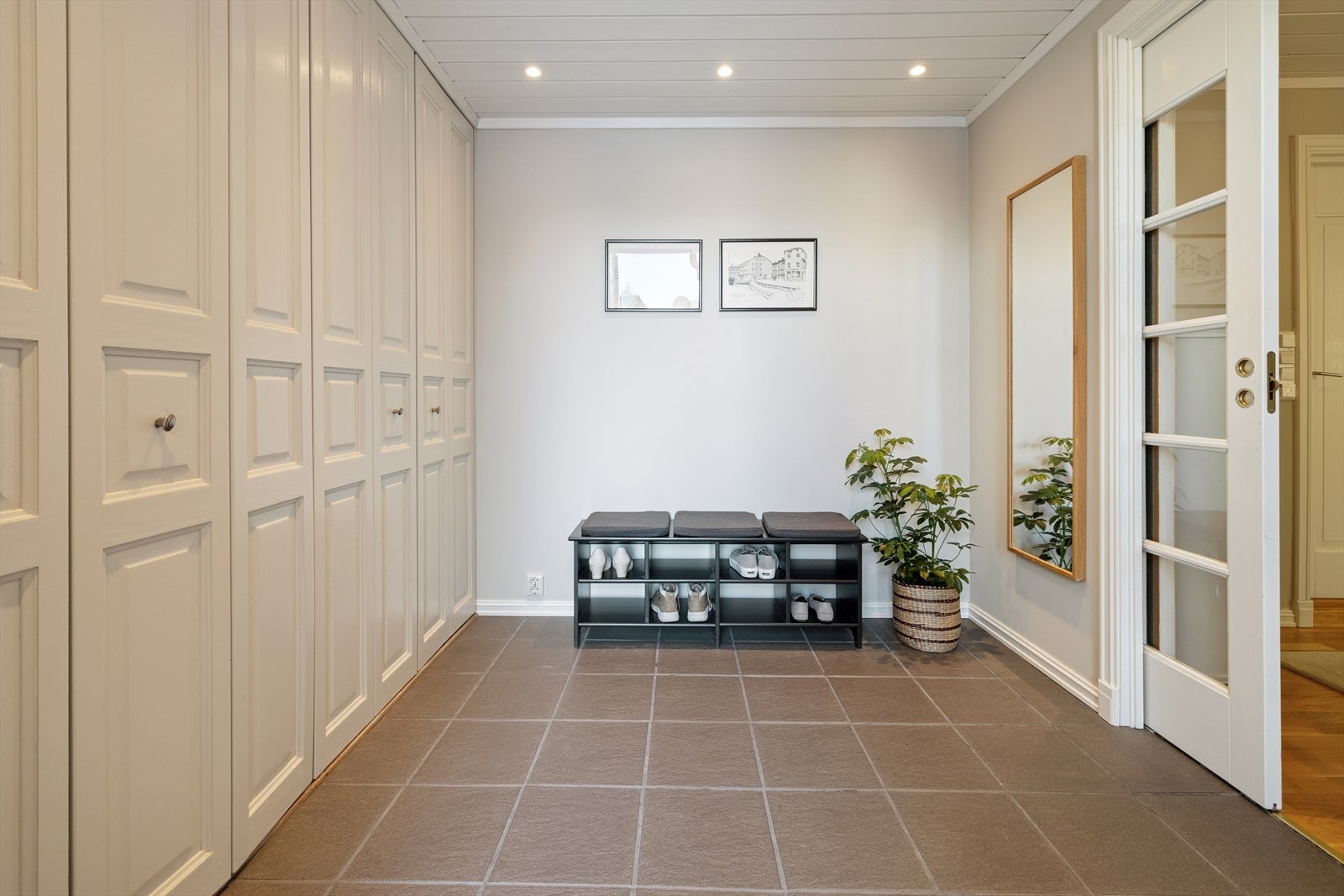En hel vegg med garderobeskap gir svært god og praktisk oppbevaringsplass, og sørger for en ryddig entré. Downlights i himlingen tilfører et moderne uttrykk og gir god belysning. Fra entréen leder en skyvedør inn til en lys og romslig mellomgang. Galleribilde