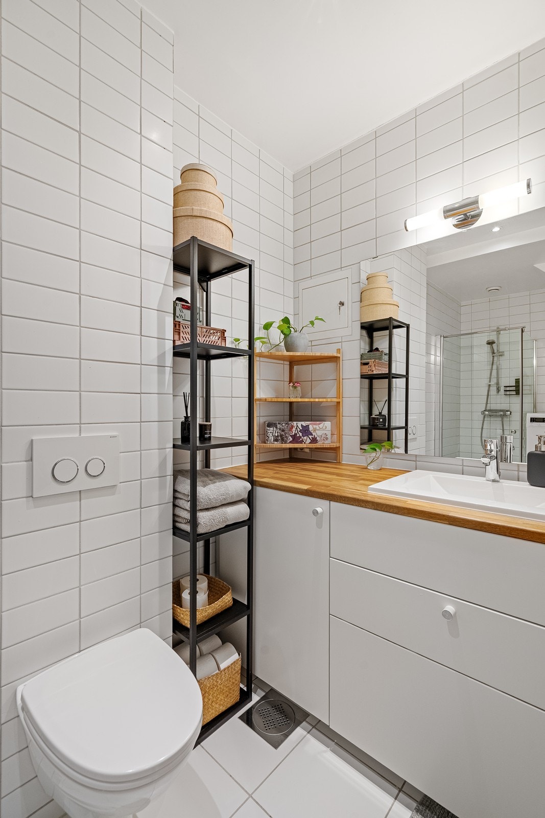 Baderomsinnredning består av servant i seksjon med speil og overlys, oppbevaring under vask, vegghengt toalett og dusjhjørne. Galleribilde