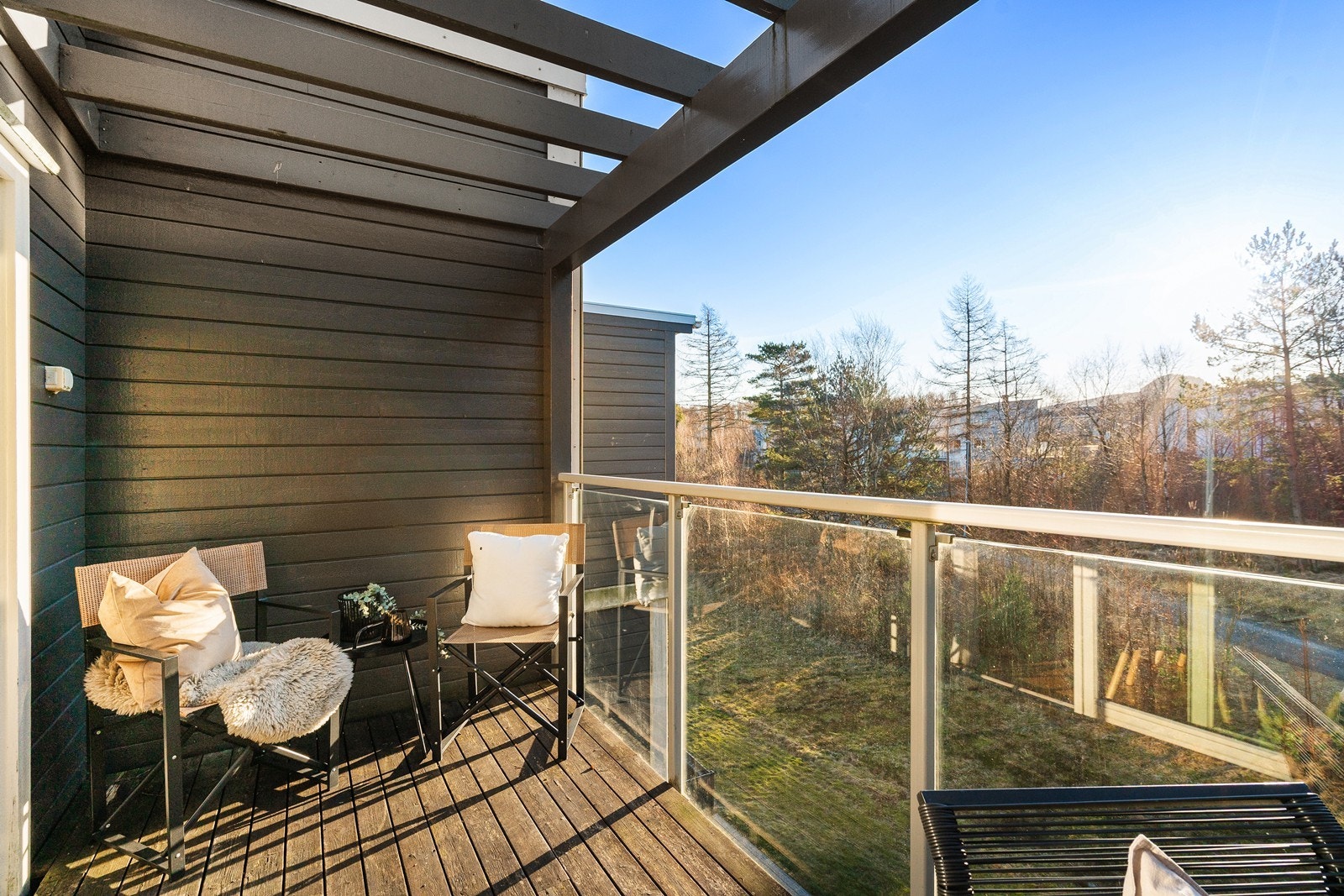 Stor sørvendt balkong utstyrt med glassrekkverk og hyggelig utsikt mot grønne omgivelser. Galleribilde