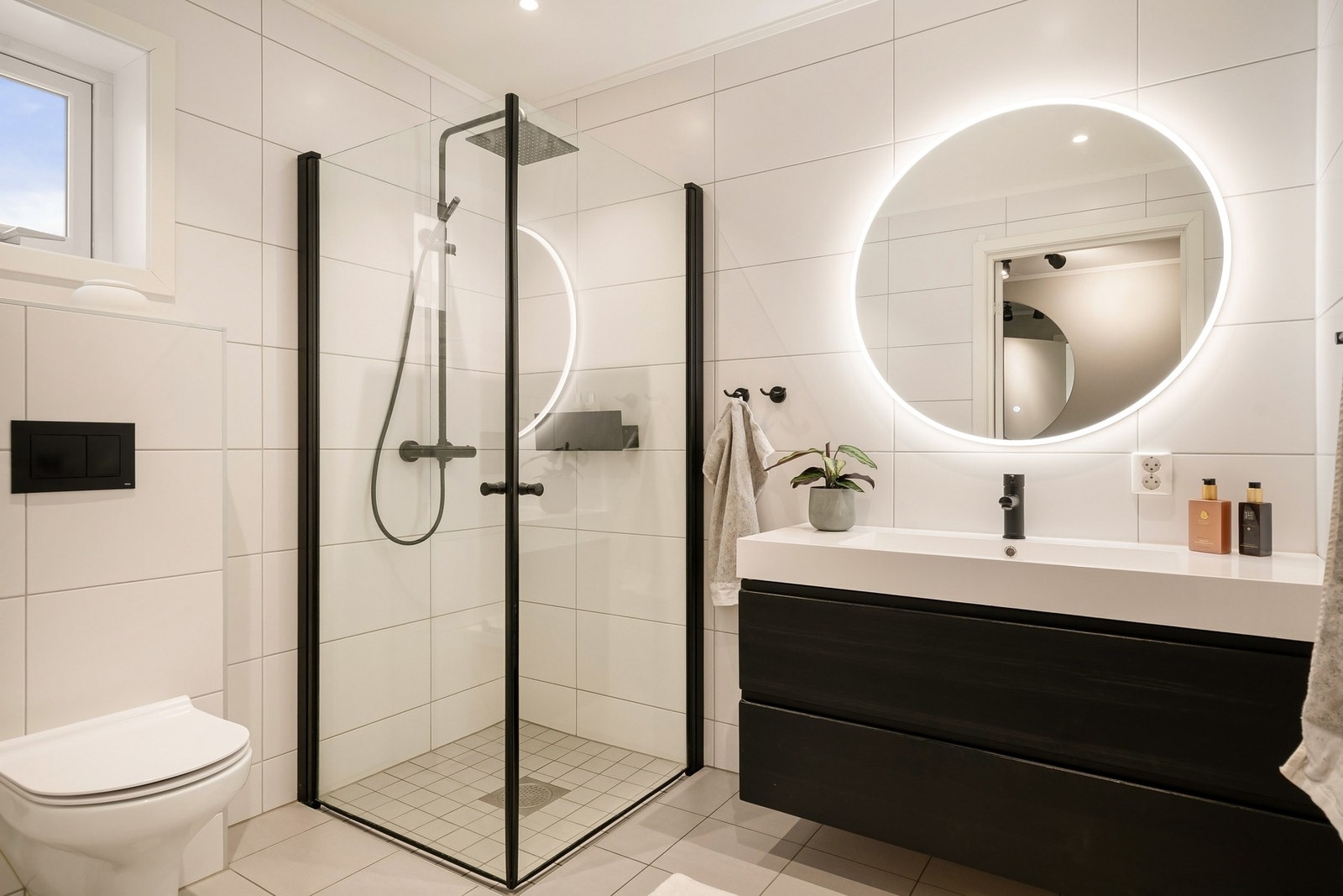 Delikat og flislagt baderom med dusjhjørne, vegghengt toalett og innredning. Galleribilde