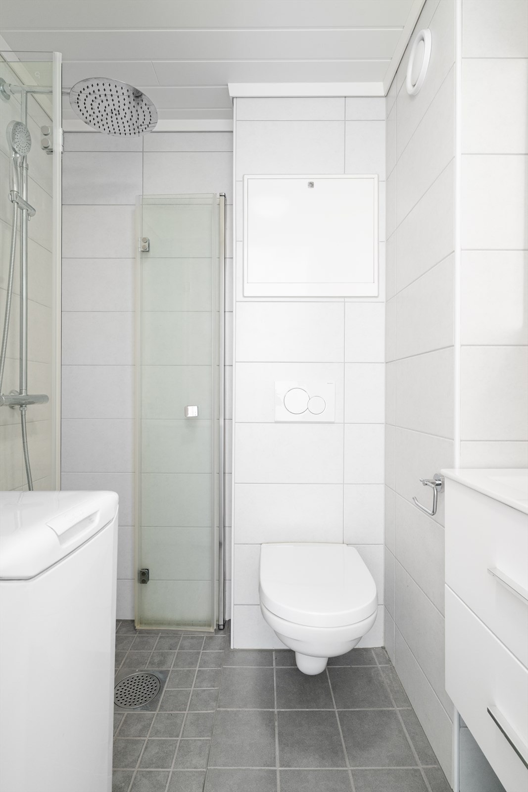 Badet er innredet med veggmontert toalett, dusjhjørne og servantinnredning med underskuffer og speilskap. Galleribilde