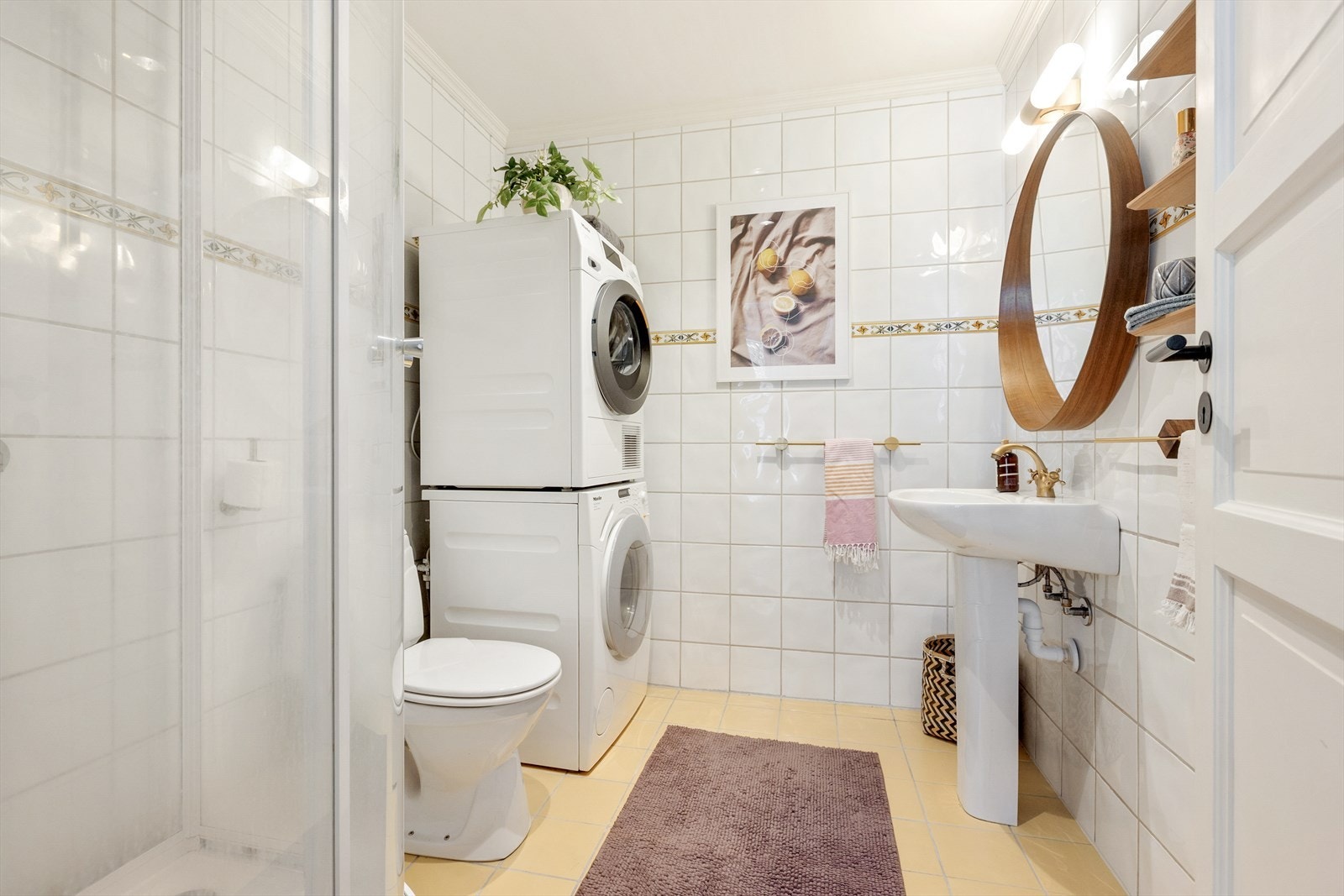 Badet har flislagte overflater, gulvvarme og opplegg for vaskemaskin. Badet inneholder dusjkabinett, toalett og servant med ett-greps blandebatteri. Galleribilde