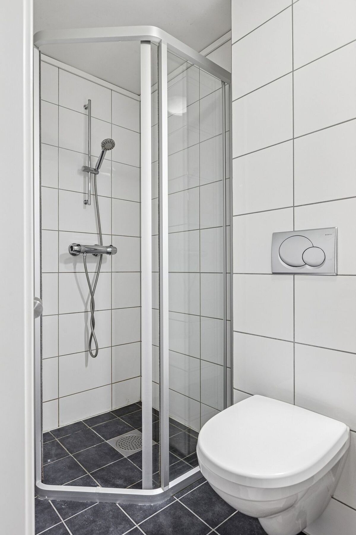 Videre er badet utstyrt med dusjhjørne, mekanisk avtrekk, opplegg for vaskemaskin, rørfordelingsskap, servantskap, stoppekran, vannmåler og veggmontert wc. Galleribilde