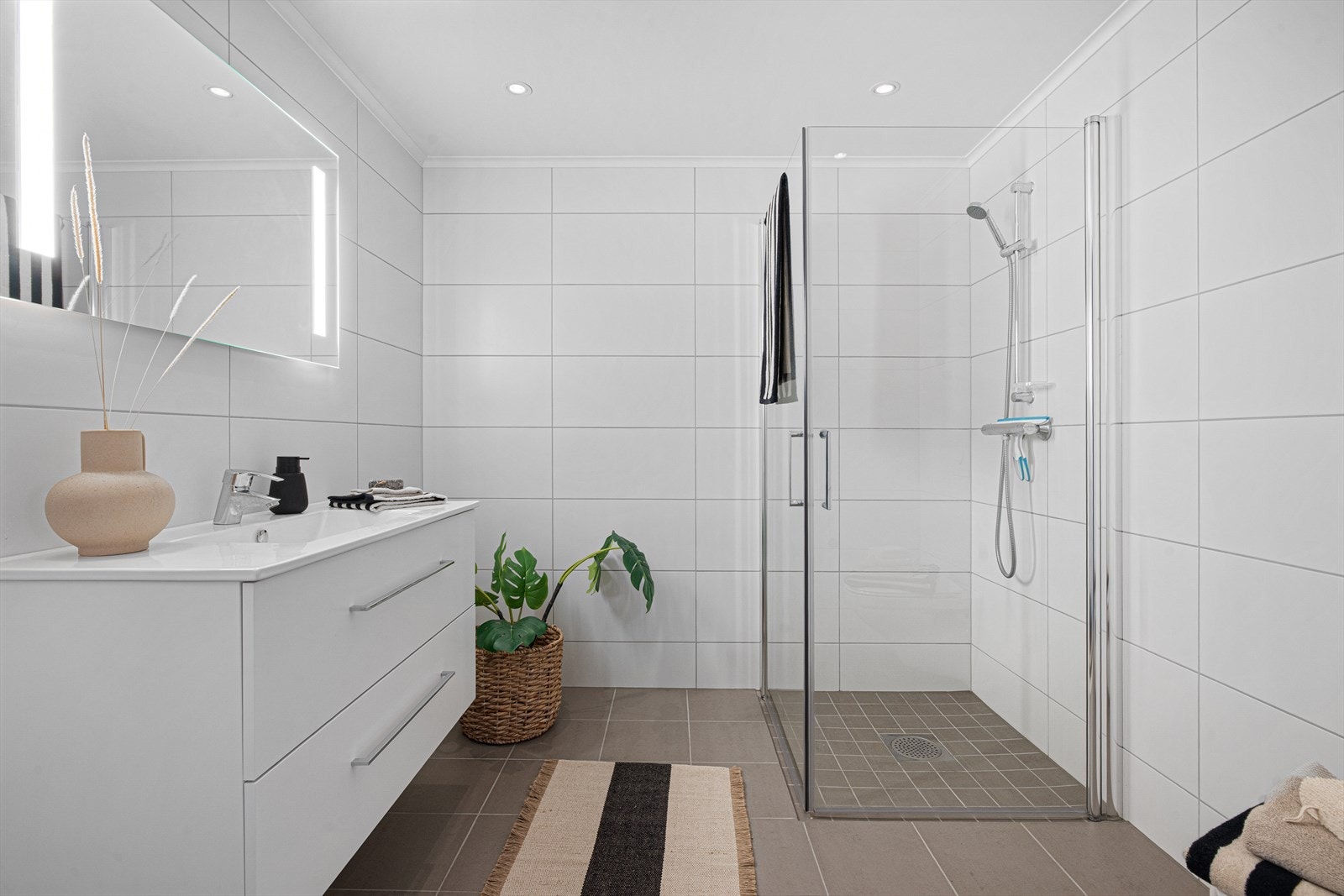 Baderommet har nøytrale fliser på vegger og gulv, med varmekabler Galleribilde