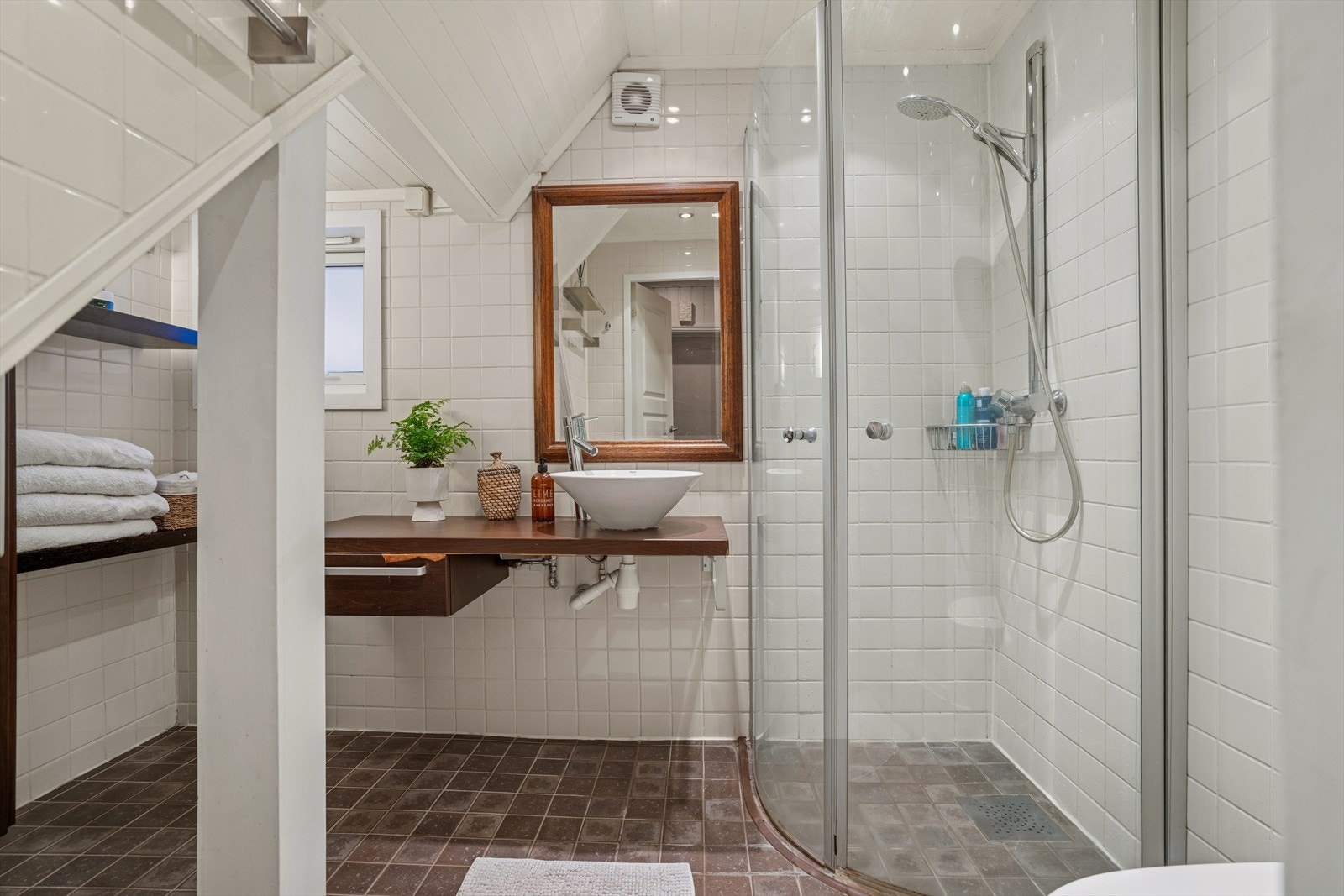 Badet er helfliset og utstyrt med varme i gulv, dusjhjørne med glassdører, servantinnredning, vegghengt speil og toalett. Galleribilde