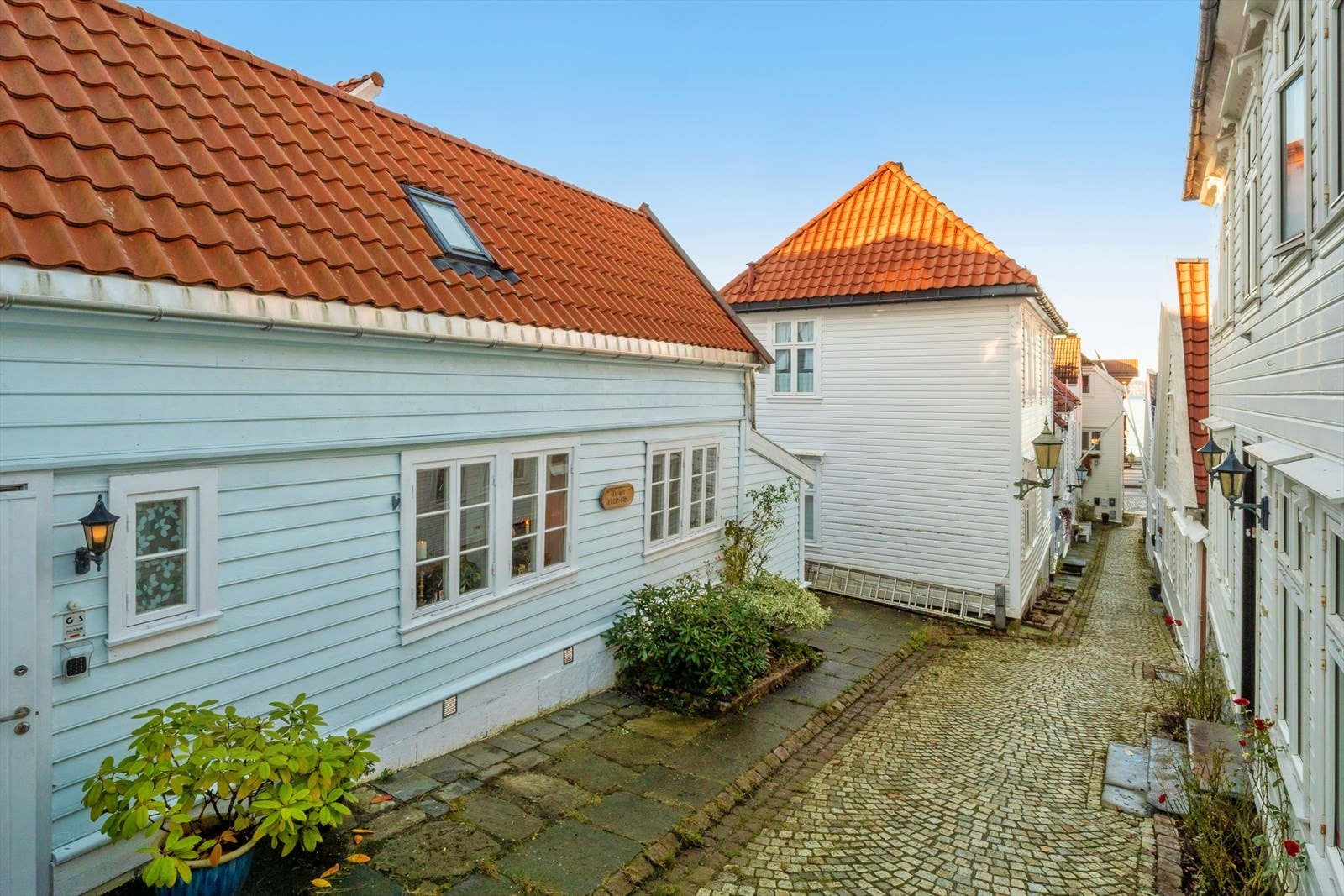 Bergens koseligste gate? Det nydelige, sjarmerende Bergenhuset er malt i en sval og lys lyseblå fargetone, med hvitmalte, profilerte vinduskarmer som fremhever husets klassiske og innbydende uttrykk og et blomsterbed hvor man kan plante blomster. Galleribilde