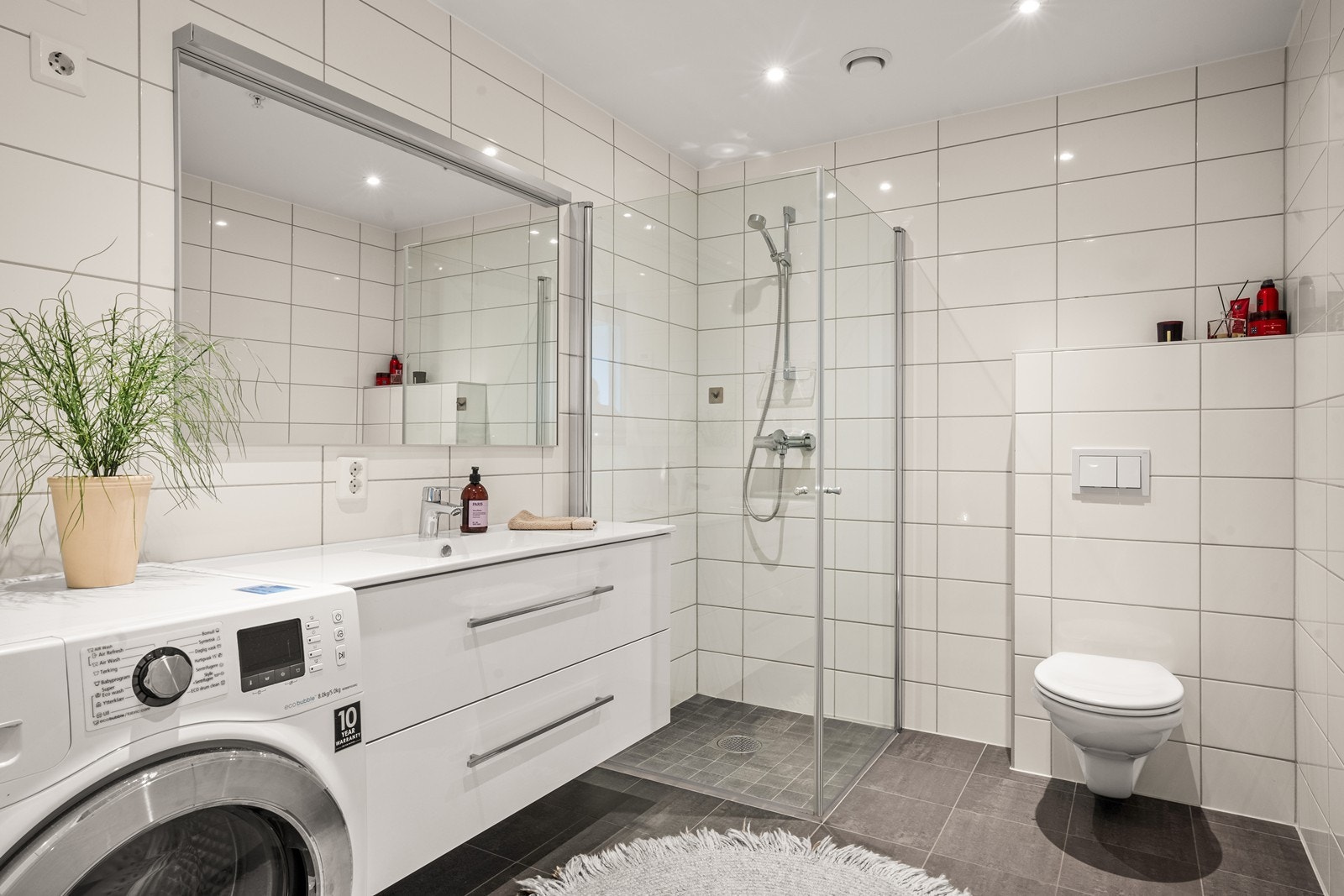 Romslig, flislagt bad med vannbåren varme, dusjhjørne og opplegg for vaskemaskin. Galleribilde