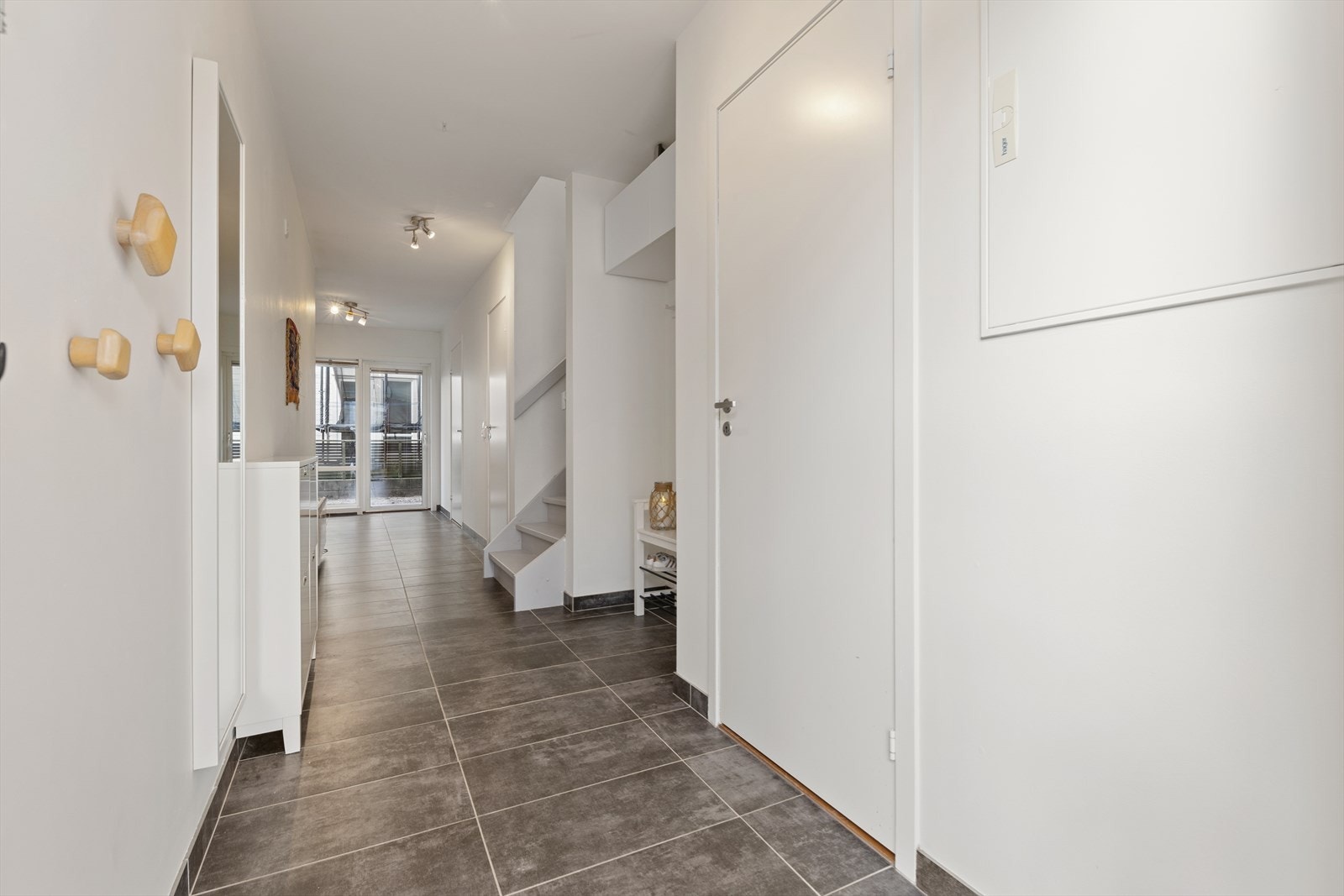 Følger man trappen ned til boligens første etasje kommer man inn i en lys og romslig gang som er praktisk innredet med flislagt gulv og garderobenisje hvor man har plass til å henge fra seg yttertøy og sko. Galleribilde