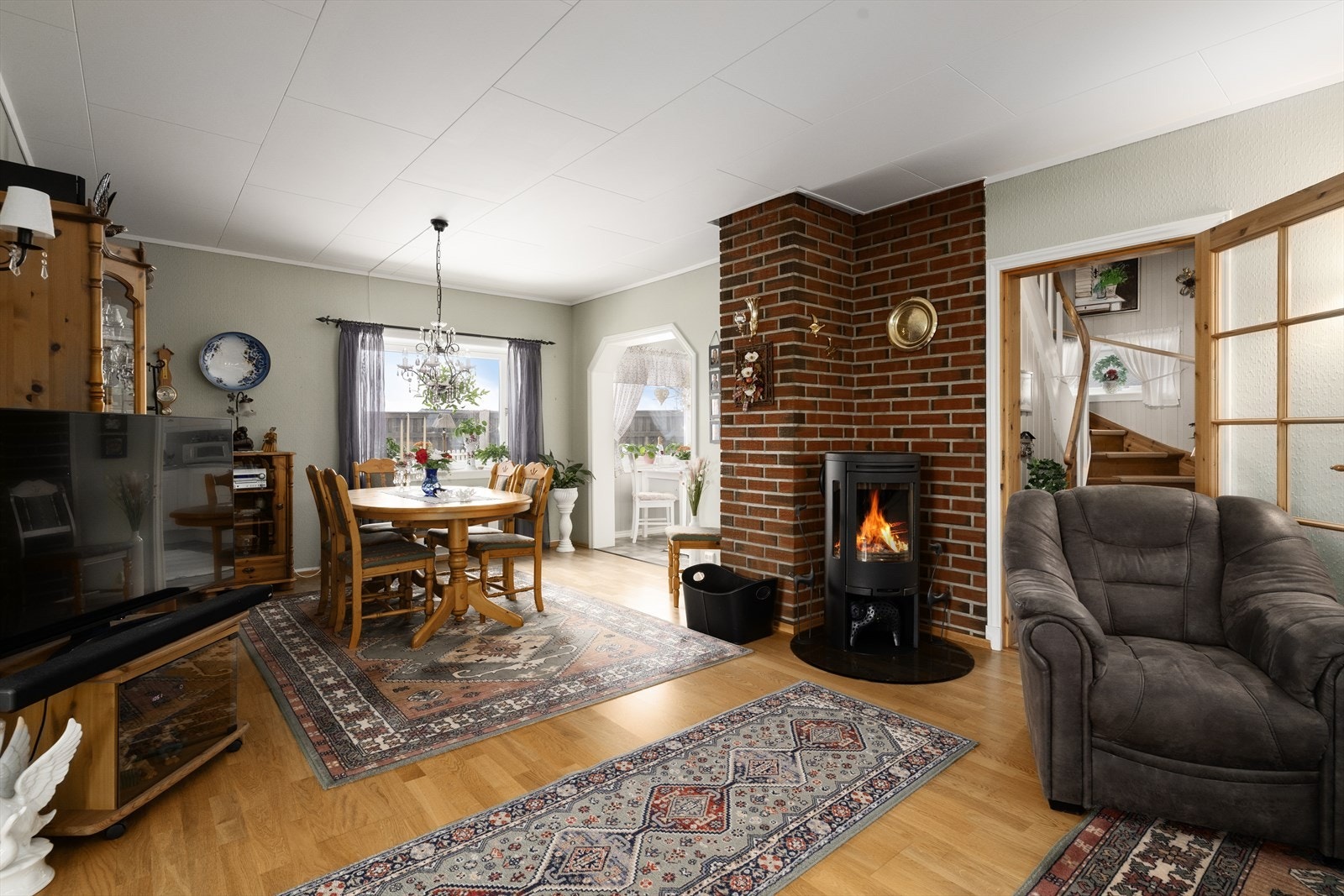 Sentralt i stua er det installert en moderne vedovn med glass på flere sider for lun varme på kjølige dager. Galleribilde