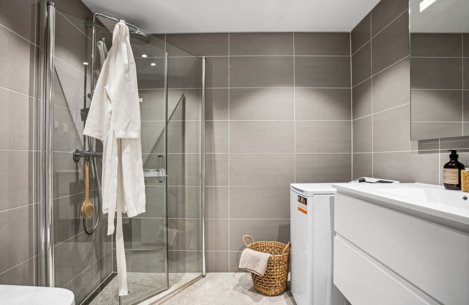 Baderomsinnredningen har stilrene skap med glatte fronter, og sanitærutstyret består av servant, veggfestet klosett og dusj på gulv. I tillegg er det praktisk opplegg for vaskemaskin, som gjør hverdagen enklere. Galleribilde