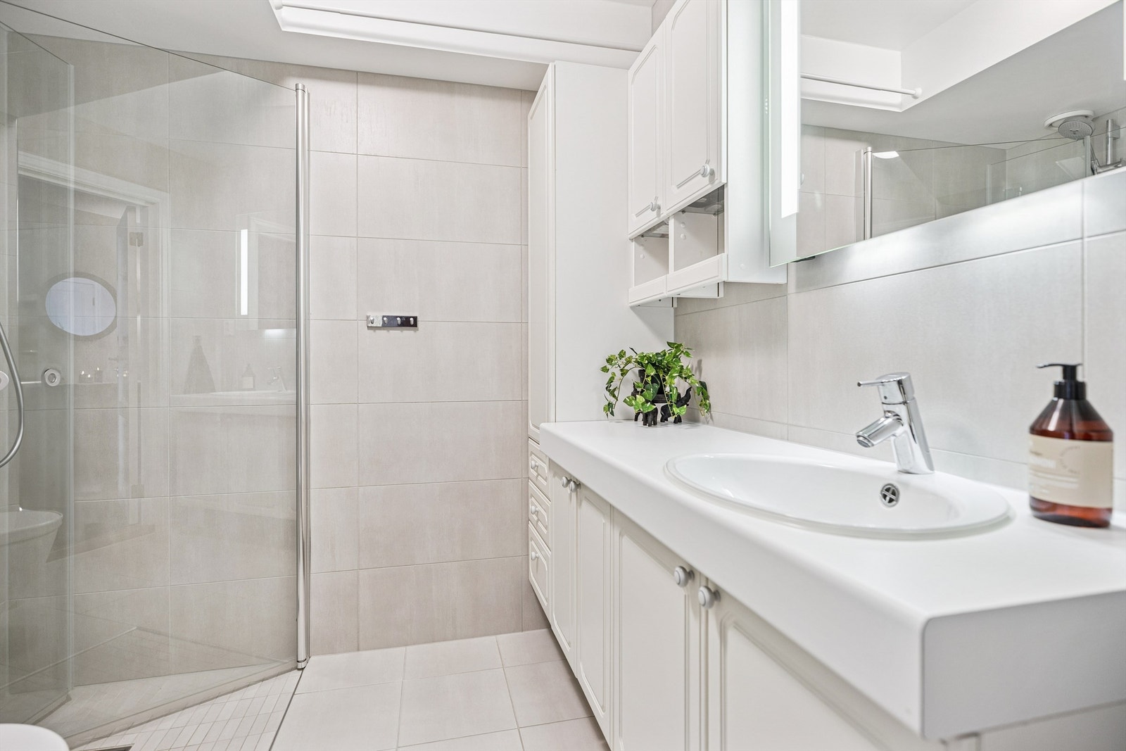 Pent flislagt bad med adkomst fra gangen. Her finner du servantinnredning, vegghengt toalett og dusjhjørne med innfellbare glassdører. Galleribilde