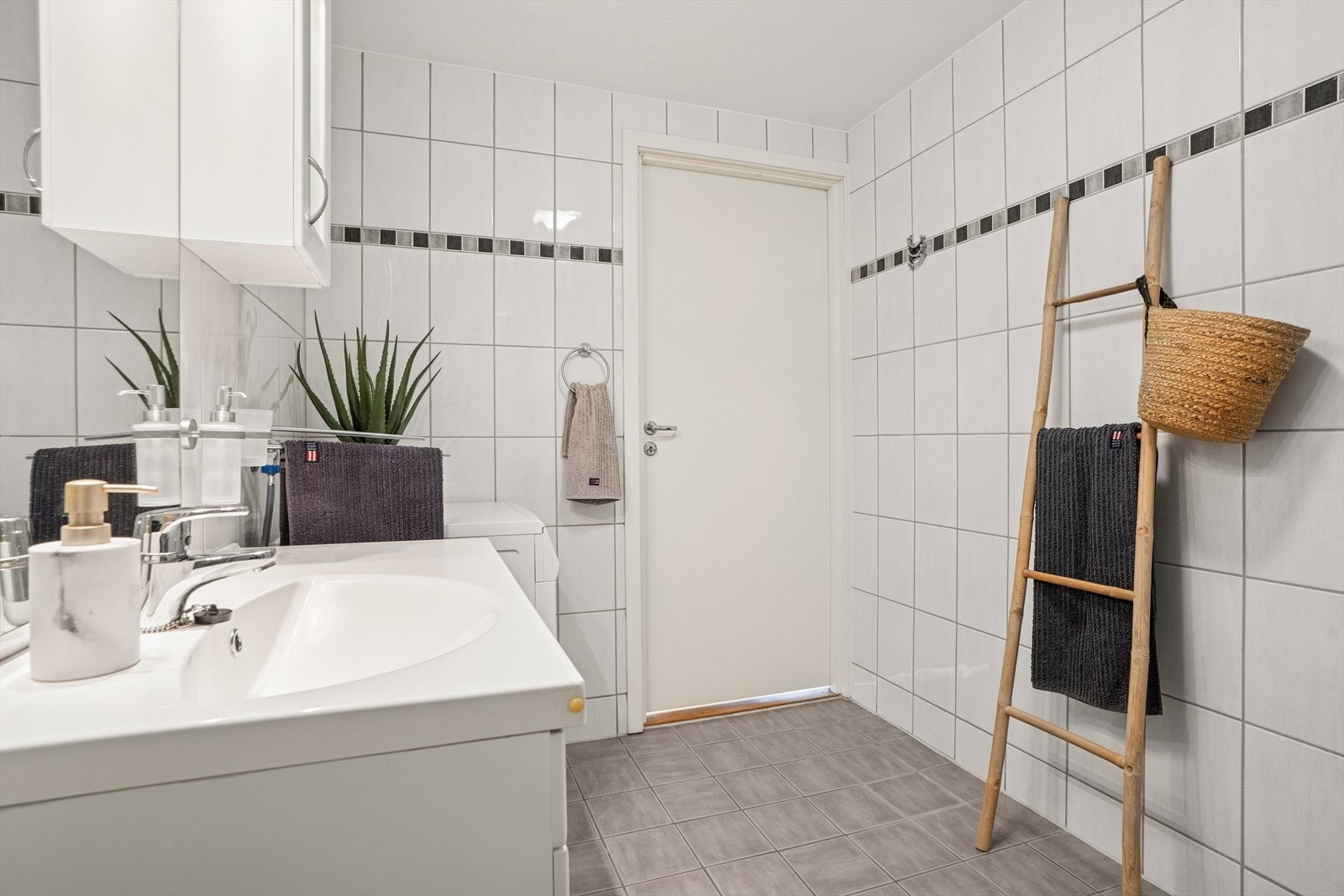 Badet fremstår som både innbydende og funksjonelt, med lyse fliser på veggene og dekorativ bård som gir et elegant uttrykk. Galleribilde