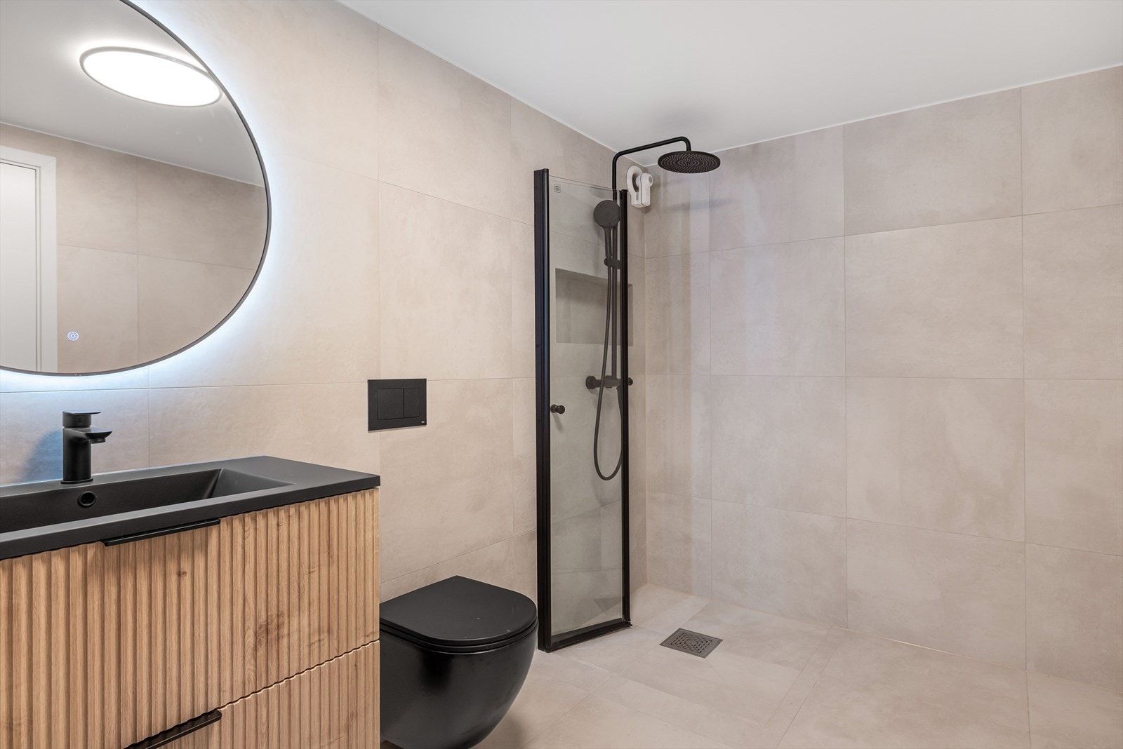 Badet har veggmontert toalett, baderomsinnredning og dusjhjørne med veggmontert dusjbatteri med regnfall. Galleribilde