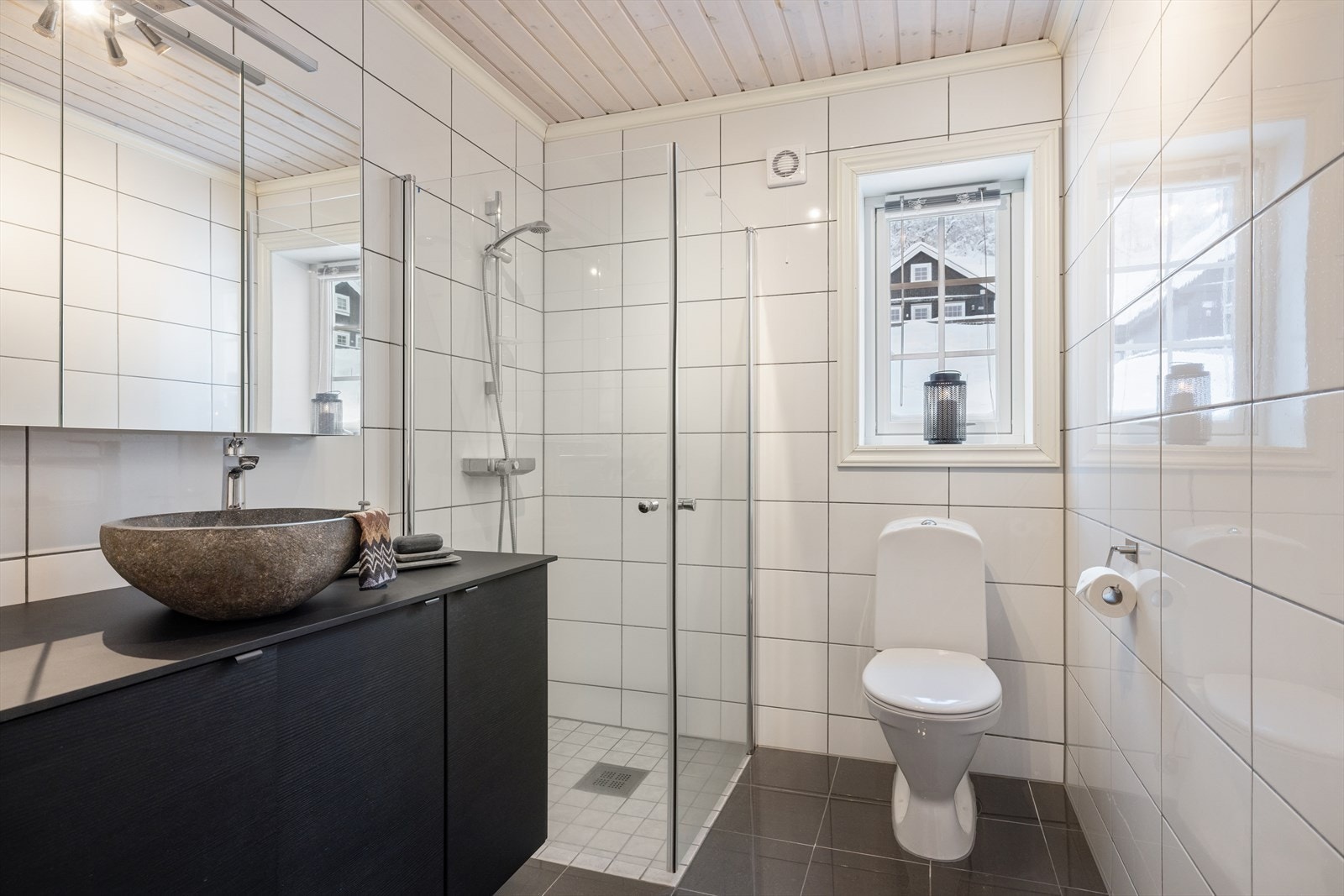 Badet er delikat flislagt på gulv og vegger, og er utstyrt med moderne baderomsinnredning, toppmontert servant og speil med integrert belysning. Galleribilde