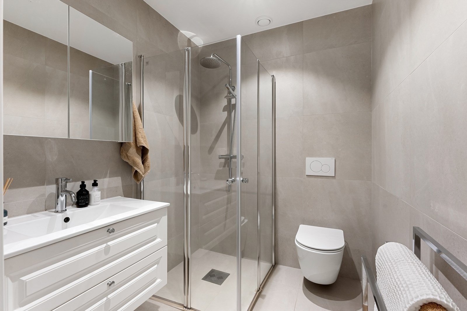 Badet er innredet med nedfelt servant, veggmontert toalett, dusjhjørne med dusjvegger samt speilskap. Galleribilde